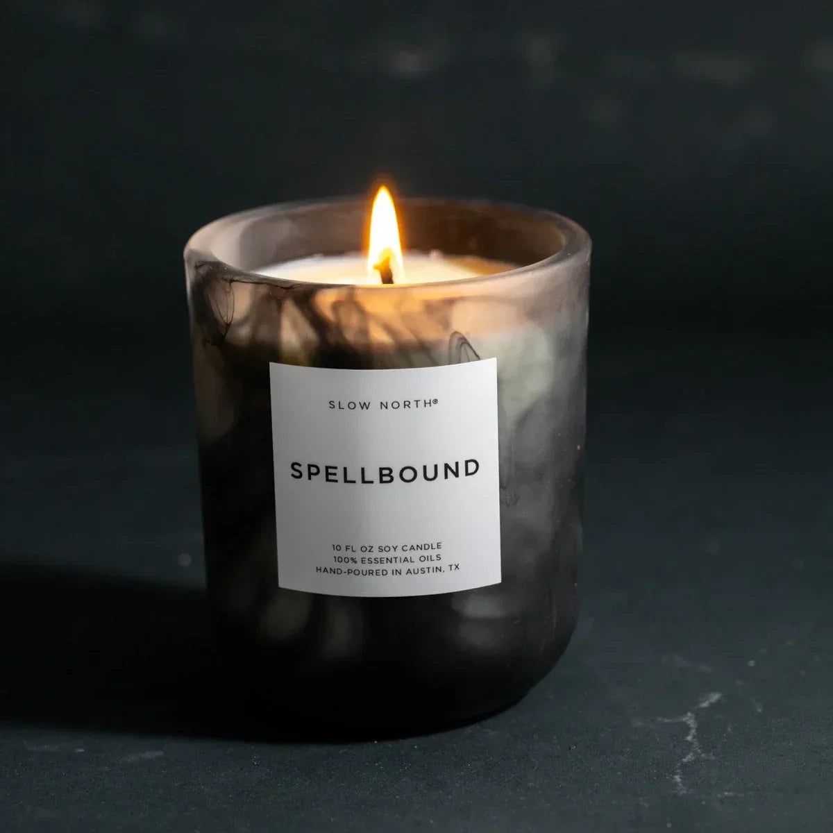Lit Spellbound soy candle in black marbled glass jar with white label on dark surface