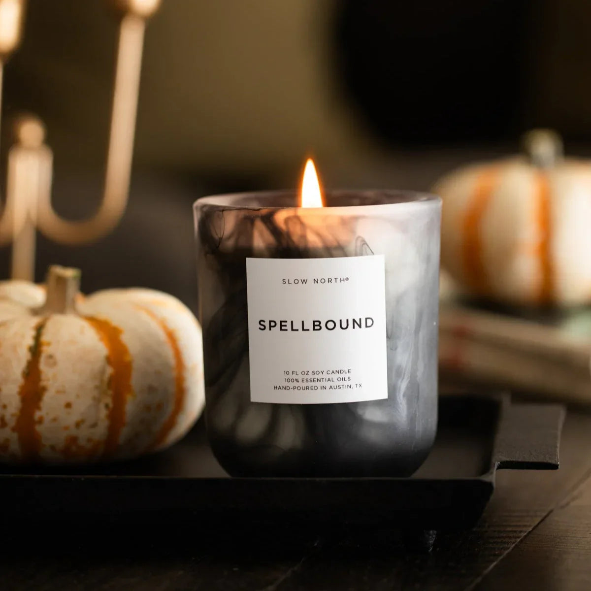 Lit Slow North Spellbound soy candle in black marble jar with white pumpkins in autumn setting