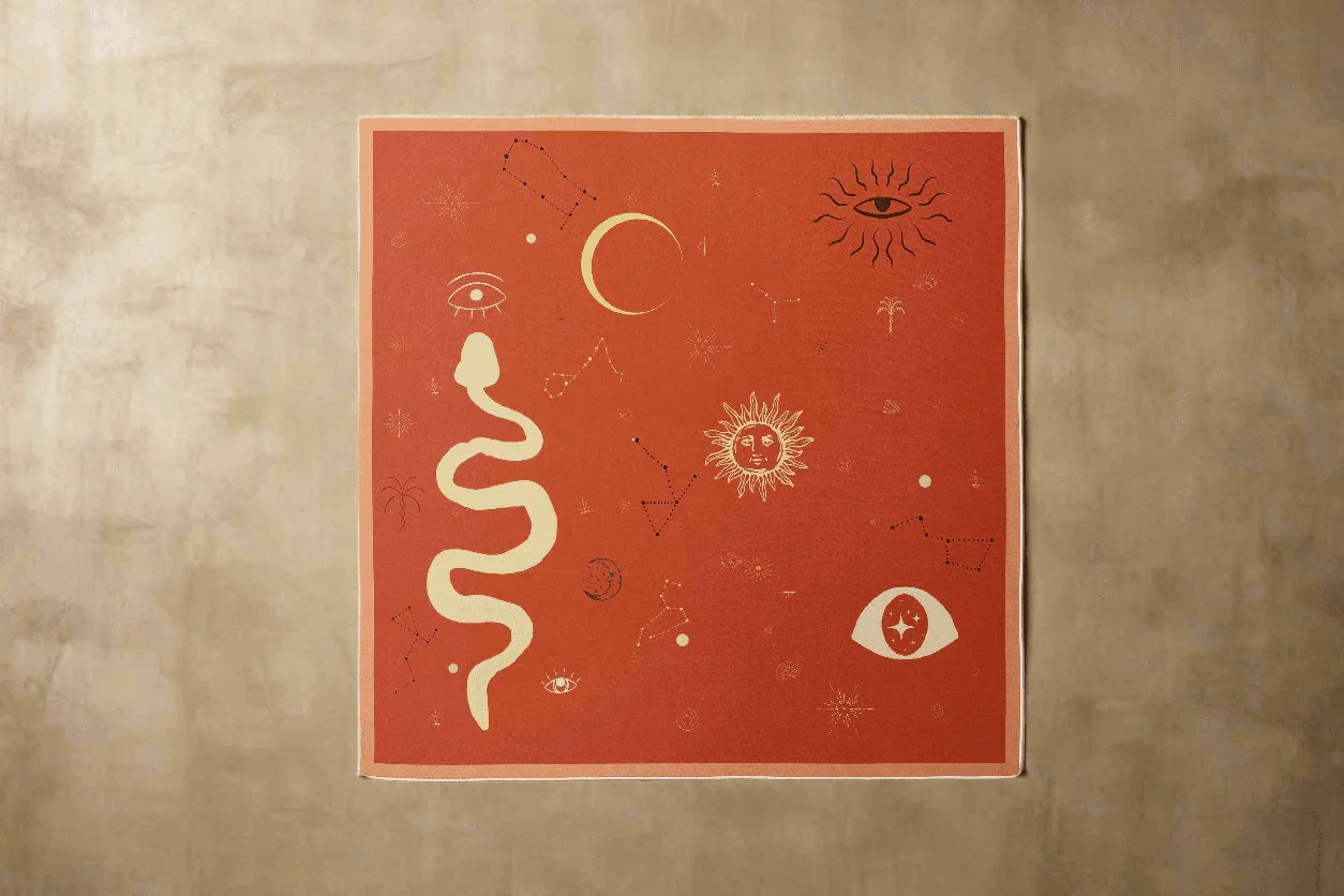Square silk scarf with celestial and mystical designs including sun, moon, eye, snake, and constellation on rust background
