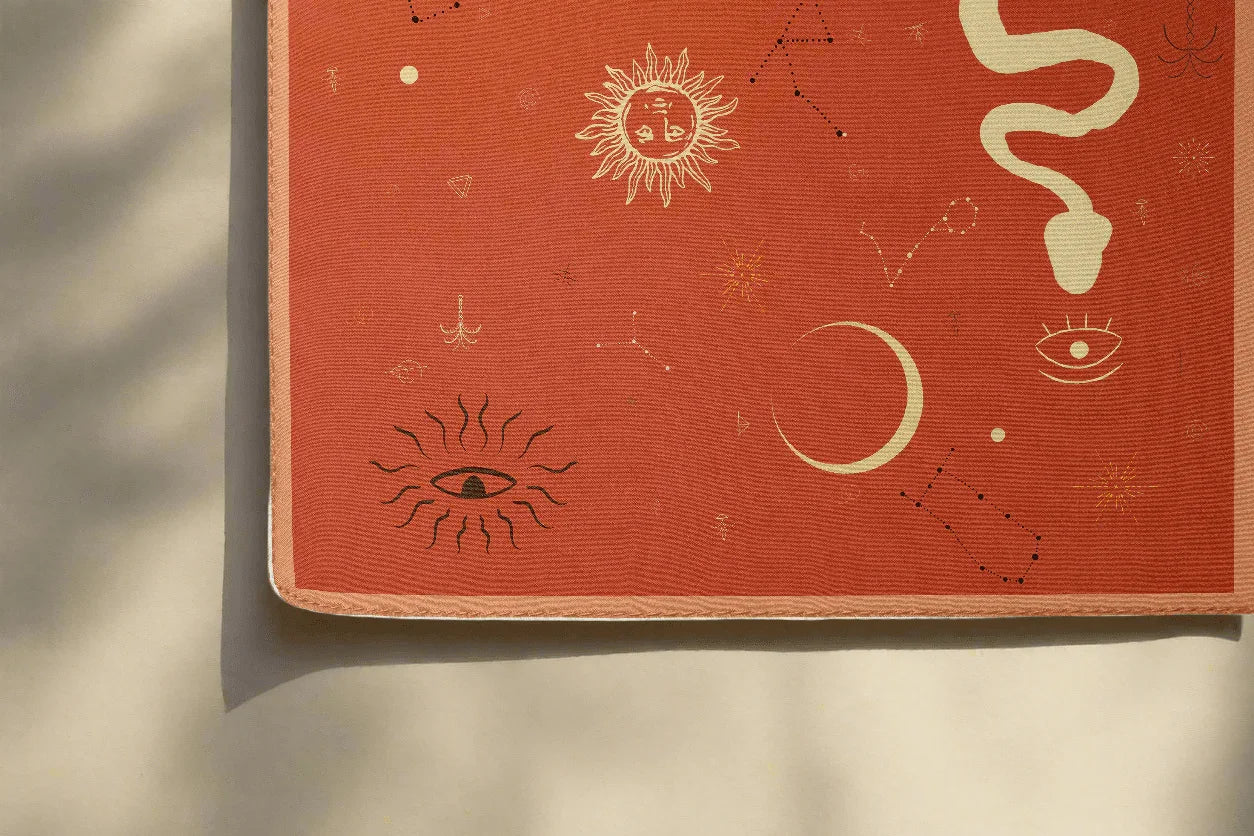 Corner of a square rust-colored silk scarf featuring celestial designs like sun, moon, stars, and snake