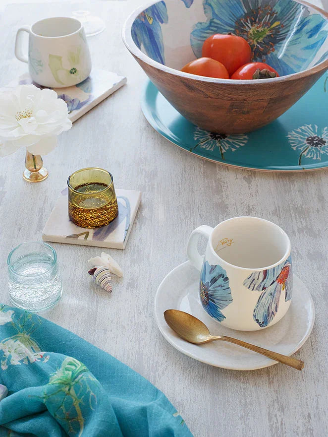 Summer tablescape with floral mug and bowl, wooden bowl with tomatoes, gold spoon, and decorative glassware on rustic table