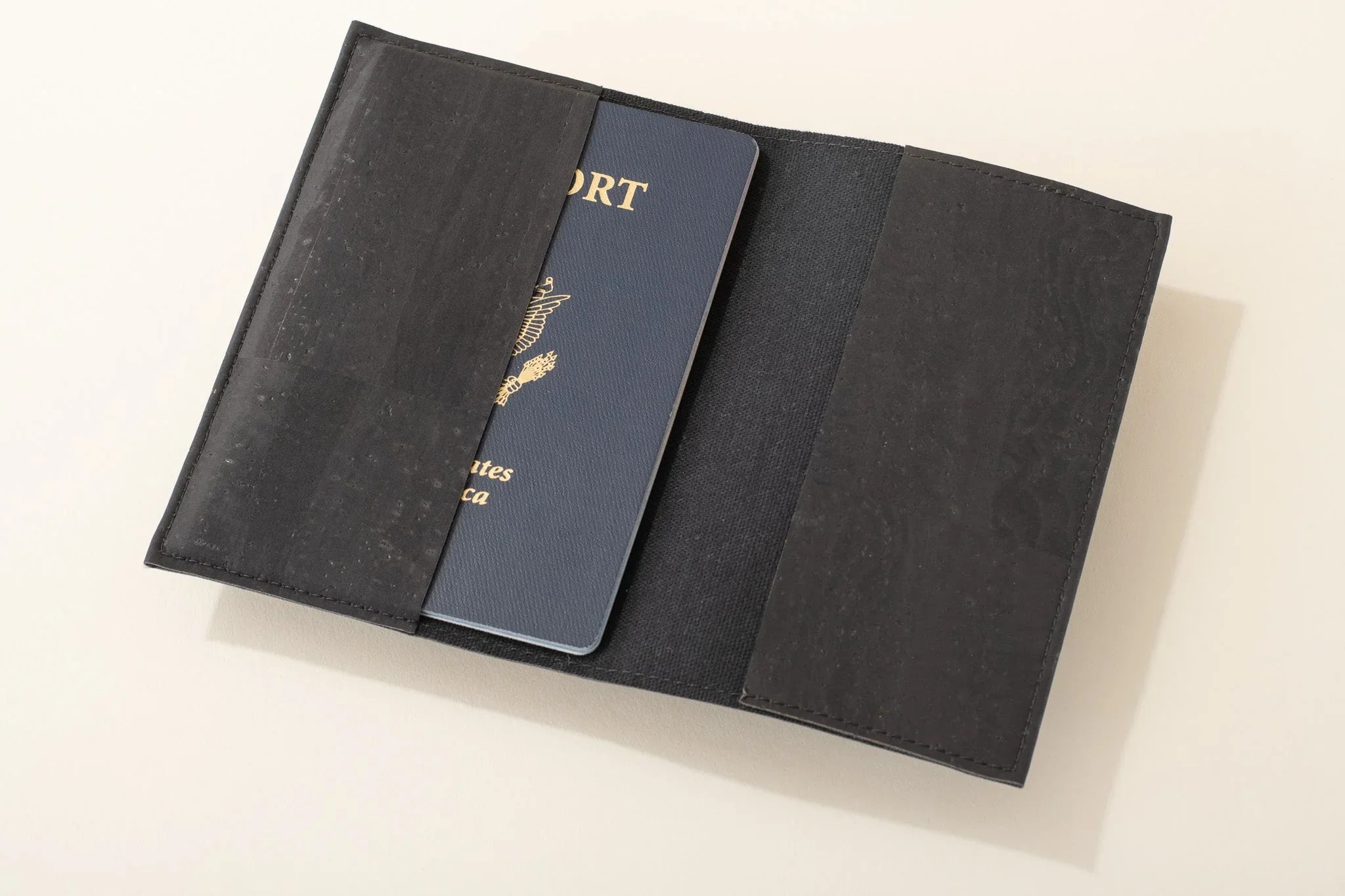 Black vegan passport holder with US passport, photographed on a light surface at Qu!rk Boutique
