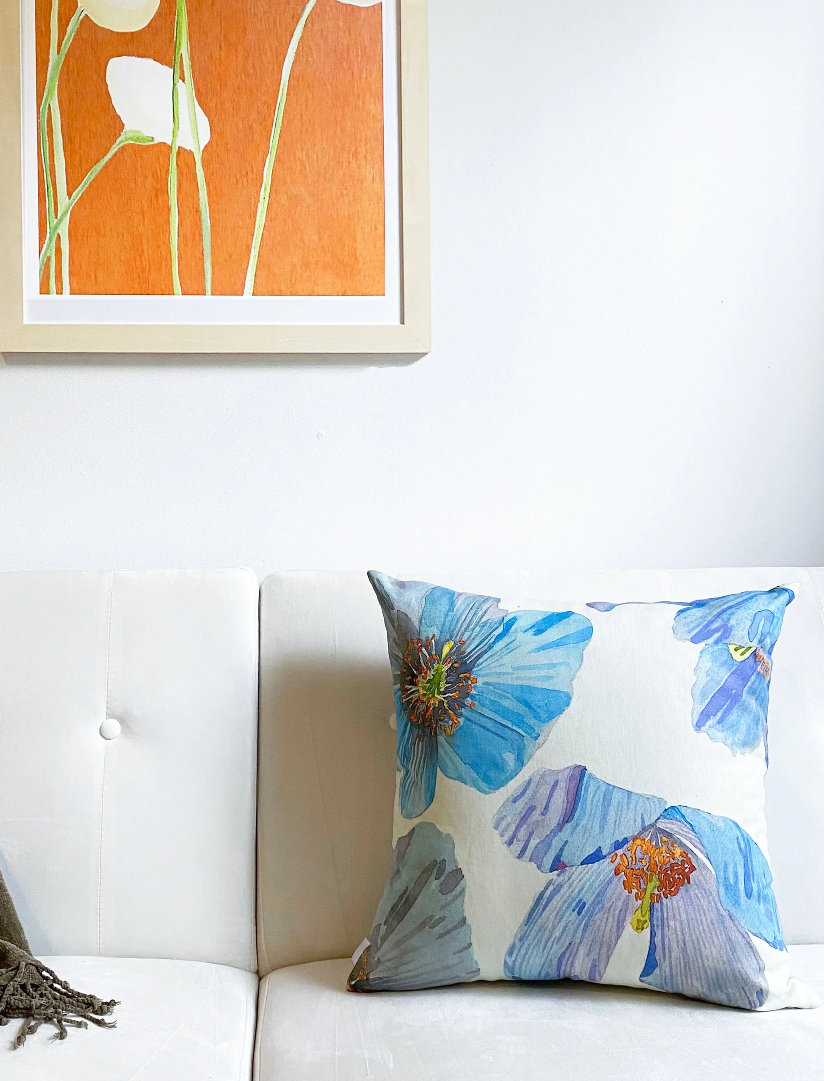 Blue floral Himalayan pillow on white modern couch with orange floral wall art