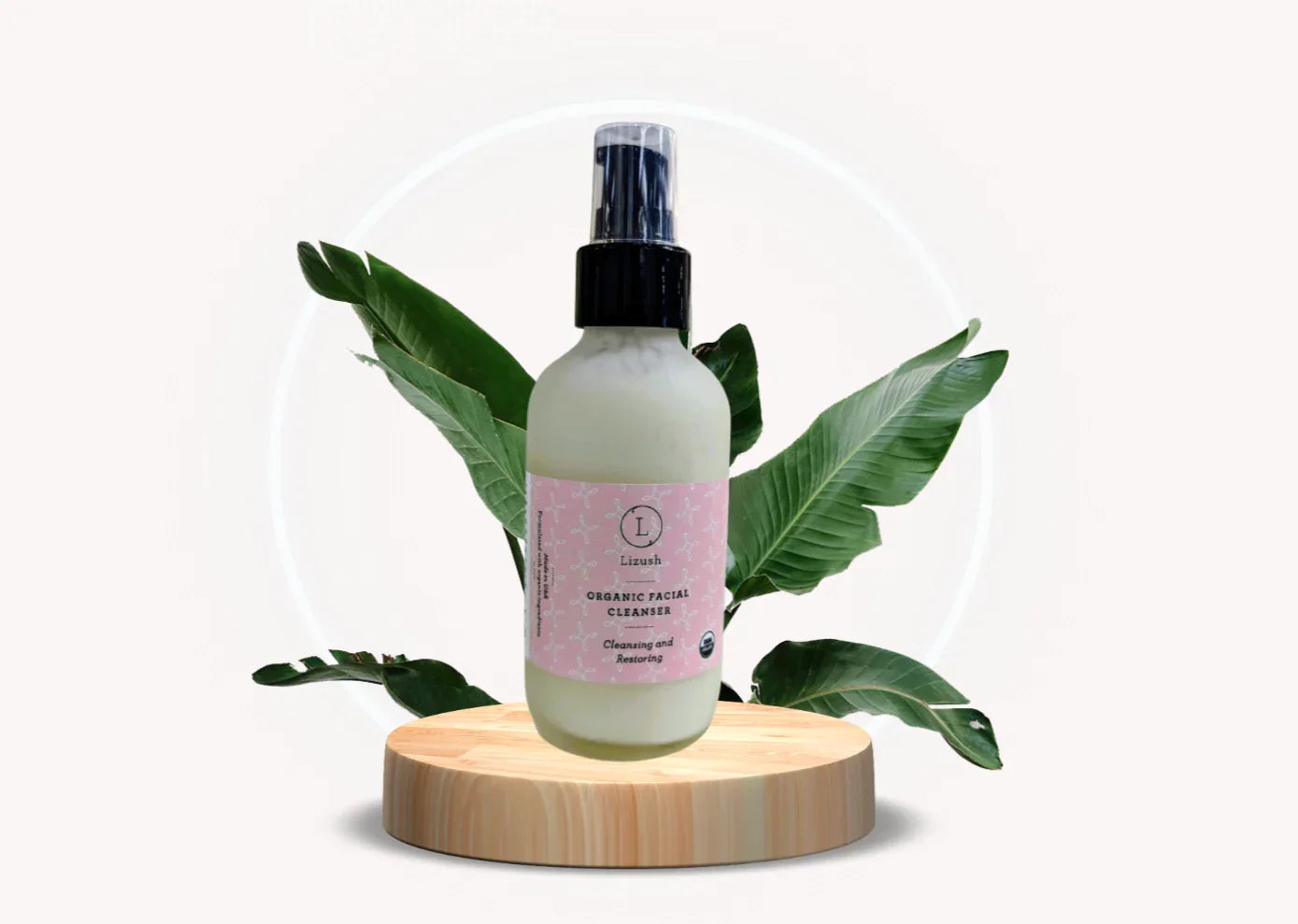 Lizush organic facial cleanser bottle with pink label on wooden platform and green leaves background