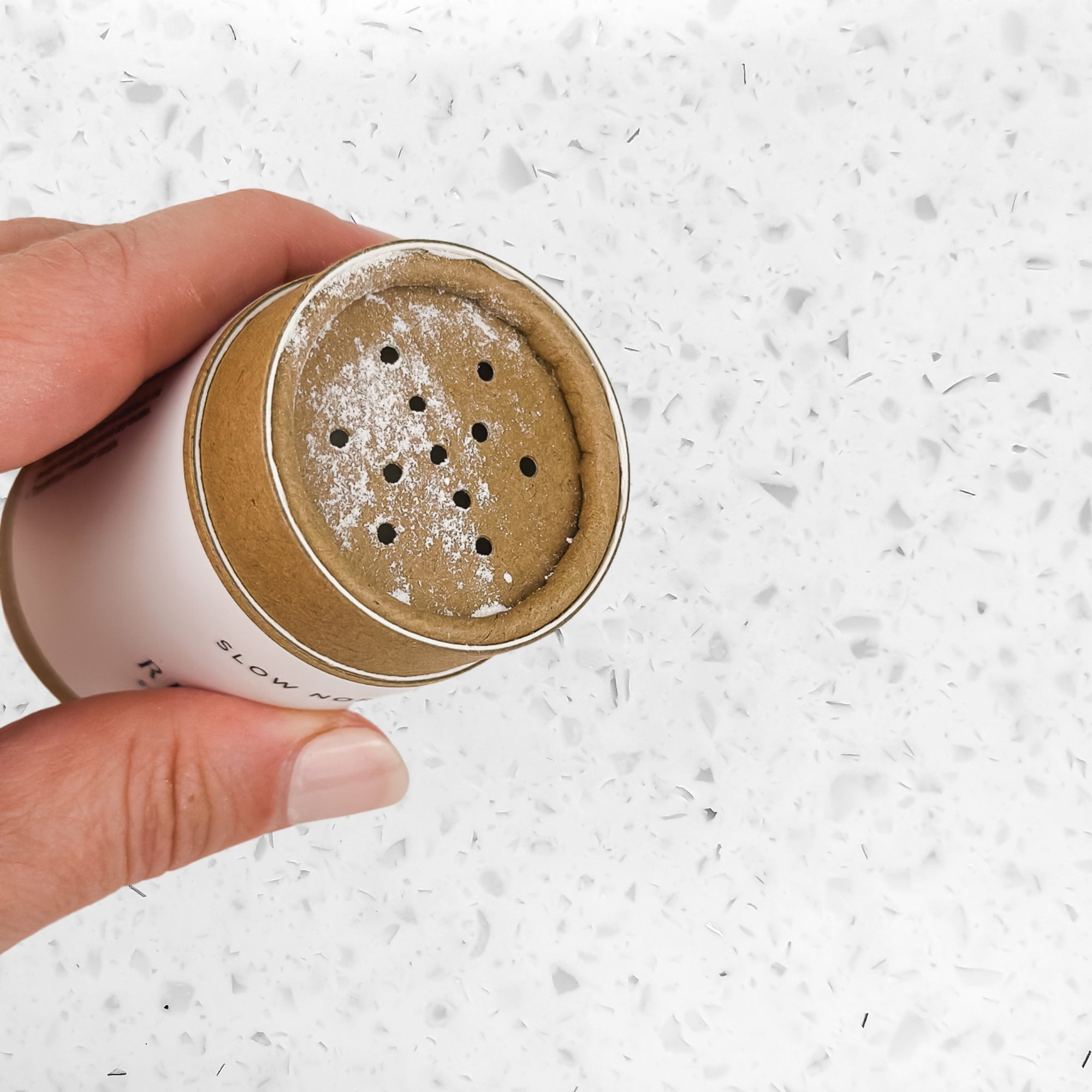 Hand holding eco-friendly cardboard dry shampoo container with powder on terrazzo surface