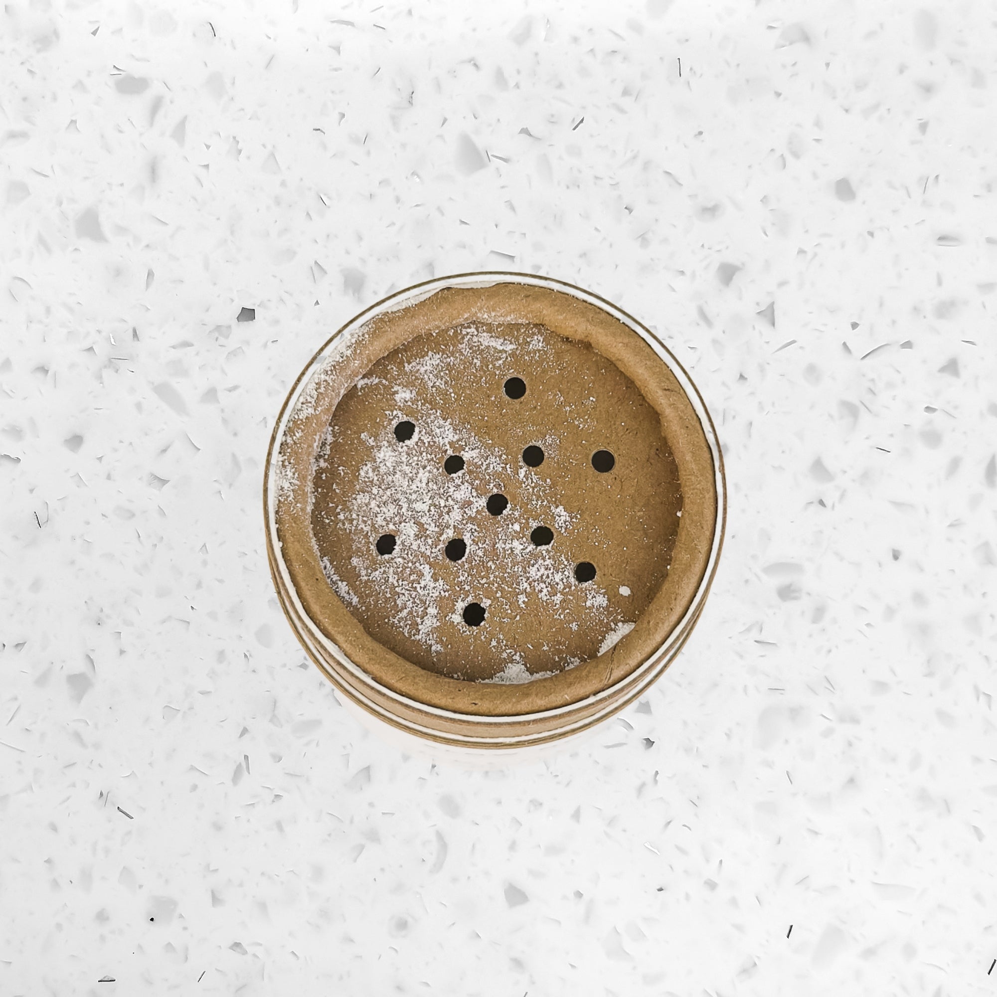 Top view of a small brown tart crust with holes on white speckled surface