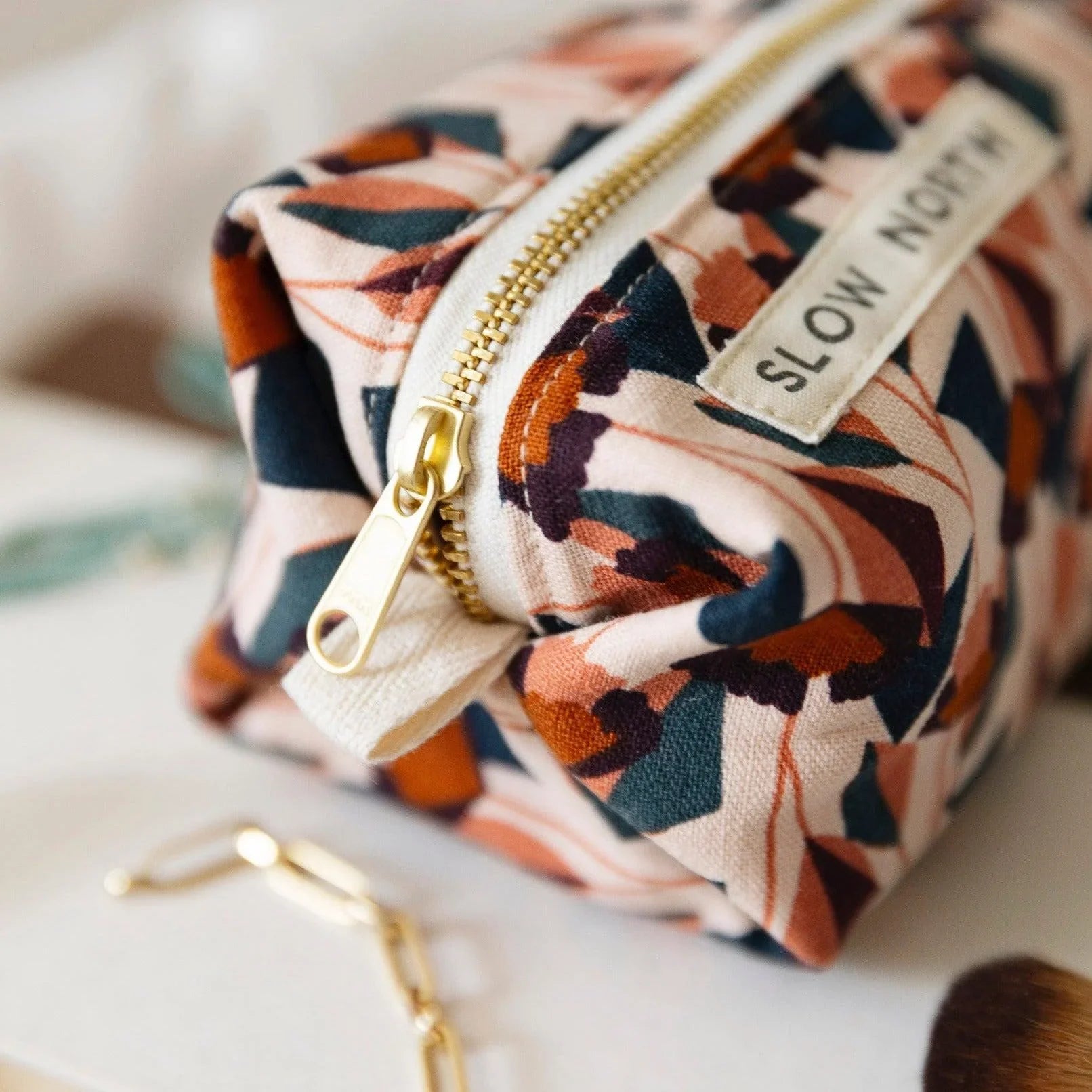 Travel pouch with blush floral print fabric and gold zipper on light surface