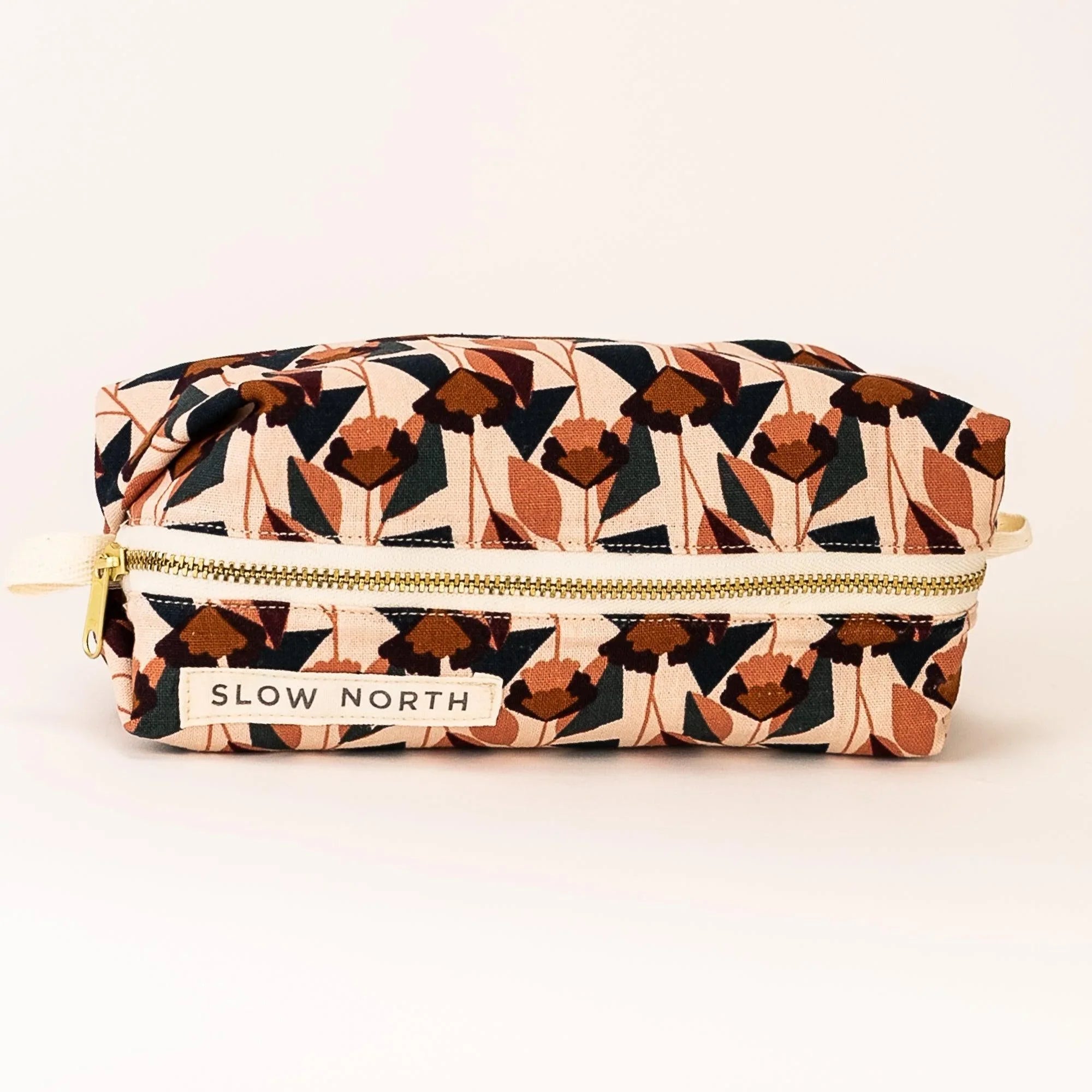 Slow North floral travel pouch with blush, brown, and black geometric pattern and gold zipper