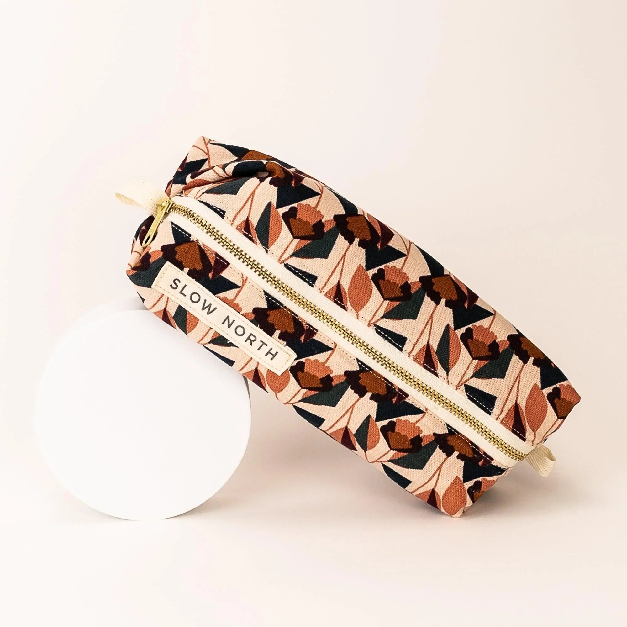 Floral patterned travel pouch with gold zipper and Slow North label on white round pedestal