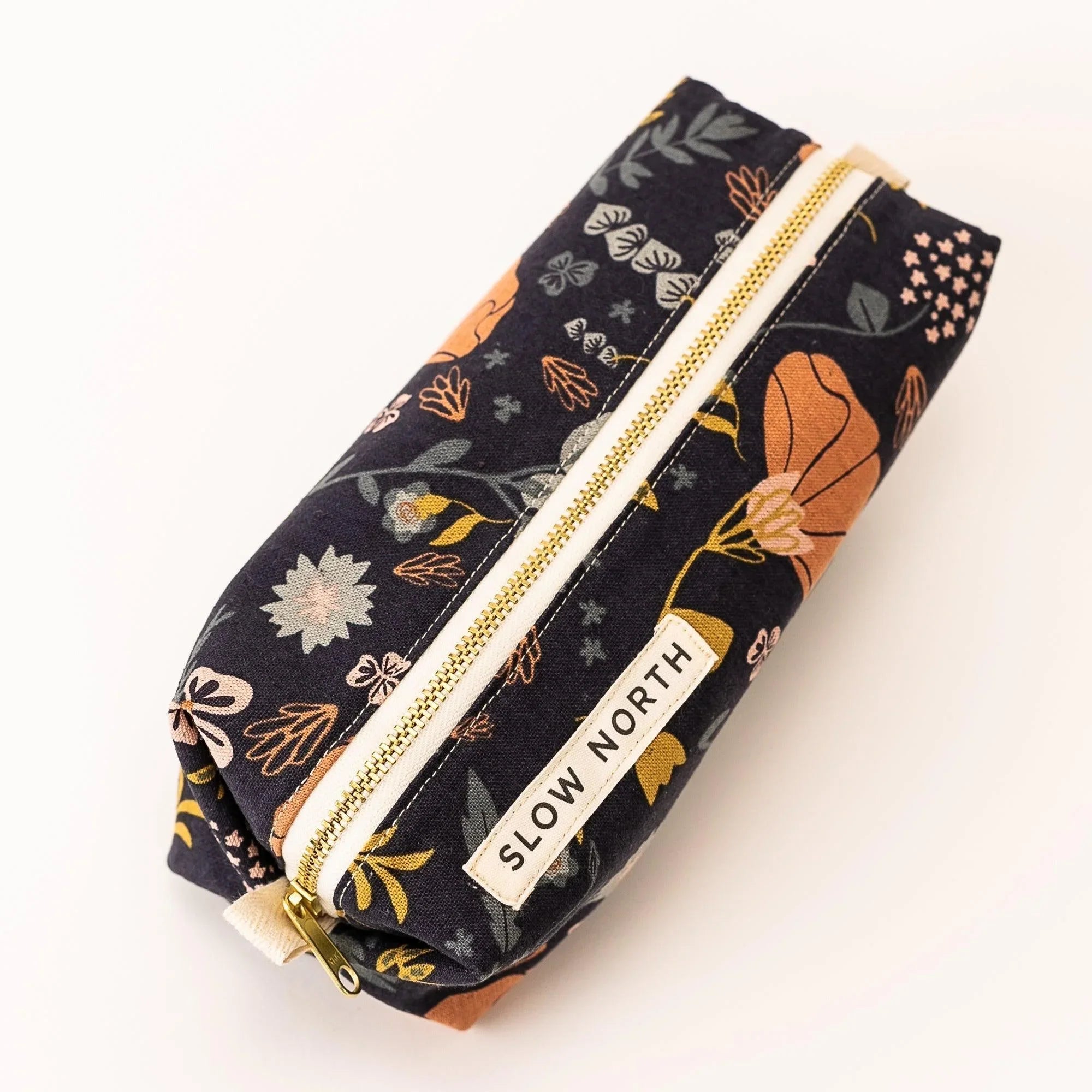 Floral-patterned travel pouch with gold zipper and Slow North label on white background