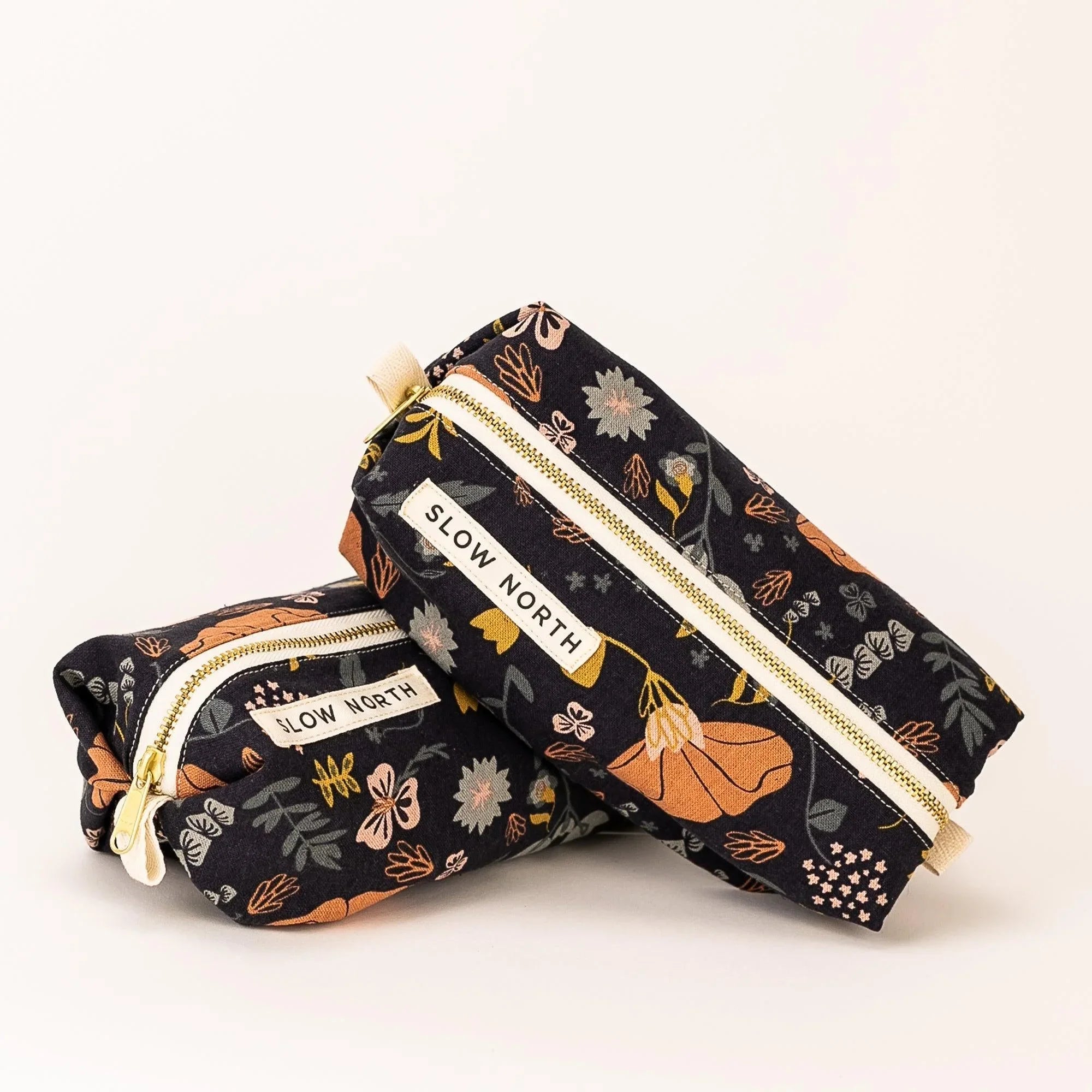 Slow North floral travel pouches with black background and beige zippers, featuring orange and gray flowers
