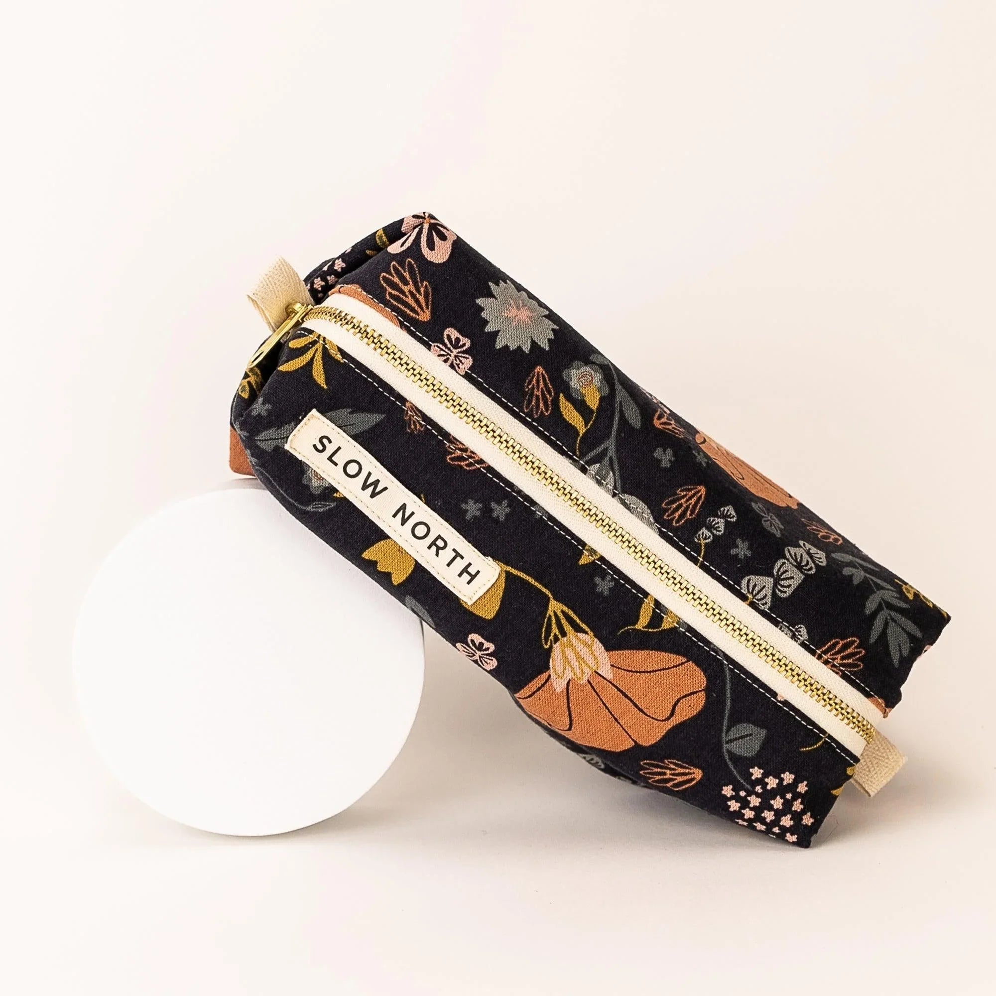 Floral patterned travel pouch with Slow North label and gold zipper on white background