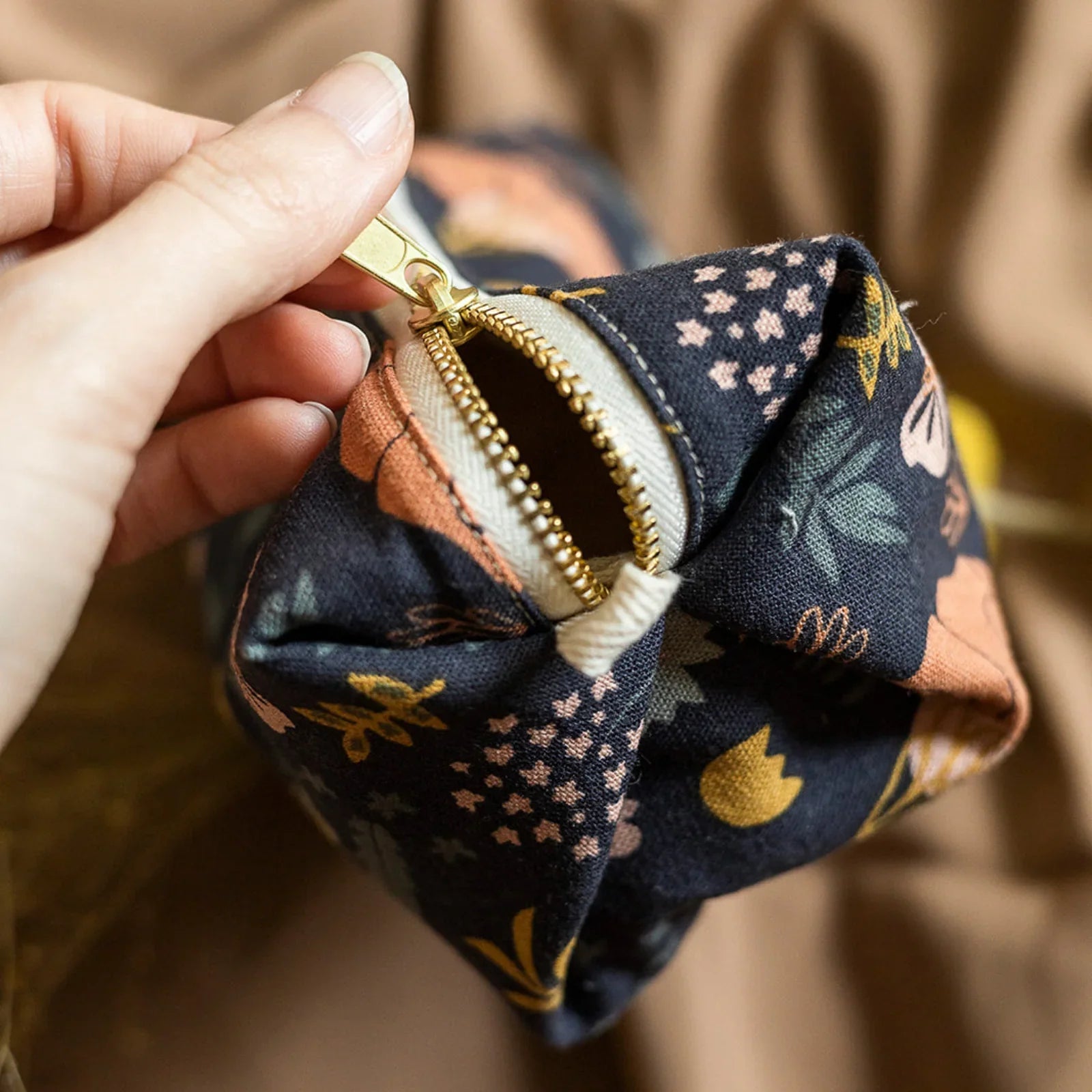 Hand opening zipper on a small fabric travel pouch with floral and leaf patterns