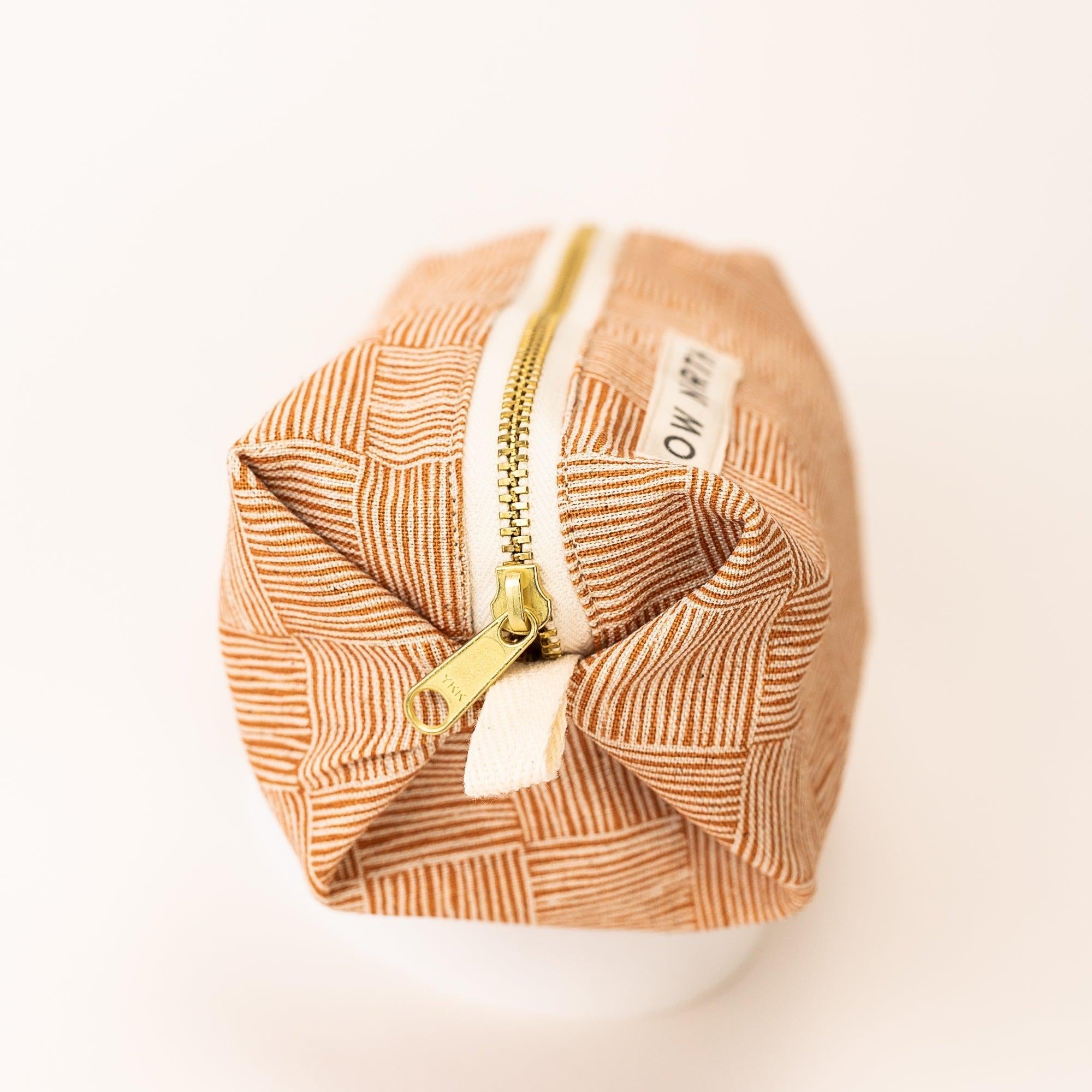 Copper-colored travel pouch with geometric stripe pattern and gold zipper on white background