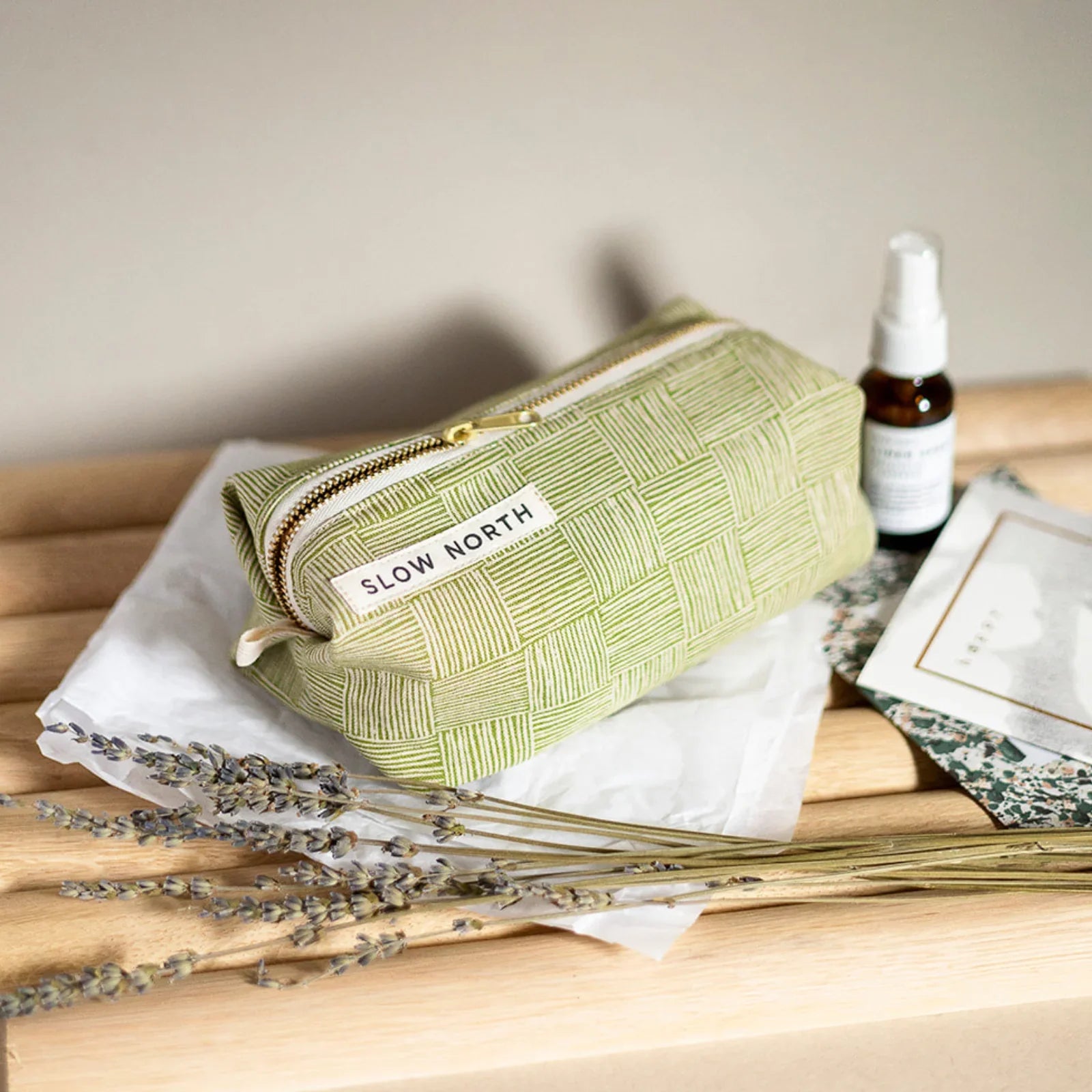 Green woven travel pouch by Slow North on wooden bench with dried lavender and spray bottle, Qu!rk Boutique