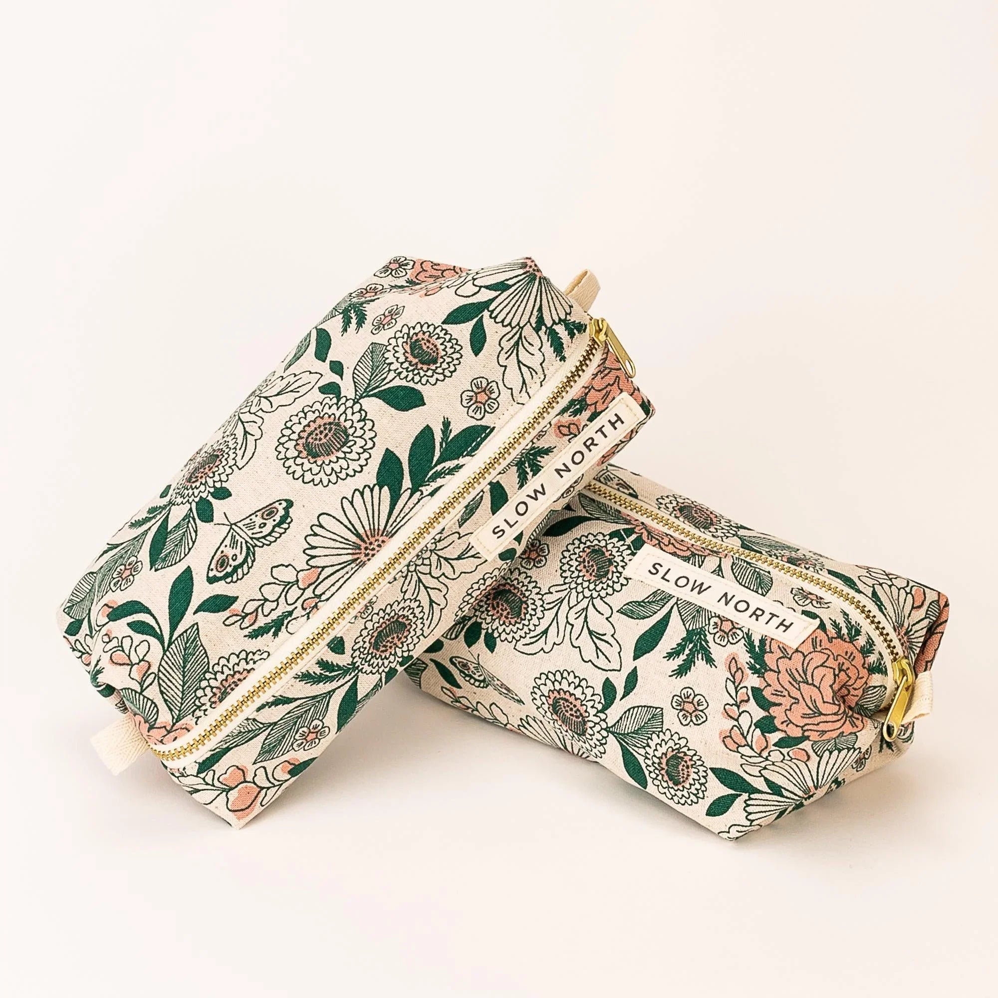 Floral travel pouches with green and peach flower design and gold zippers labeled Slow North