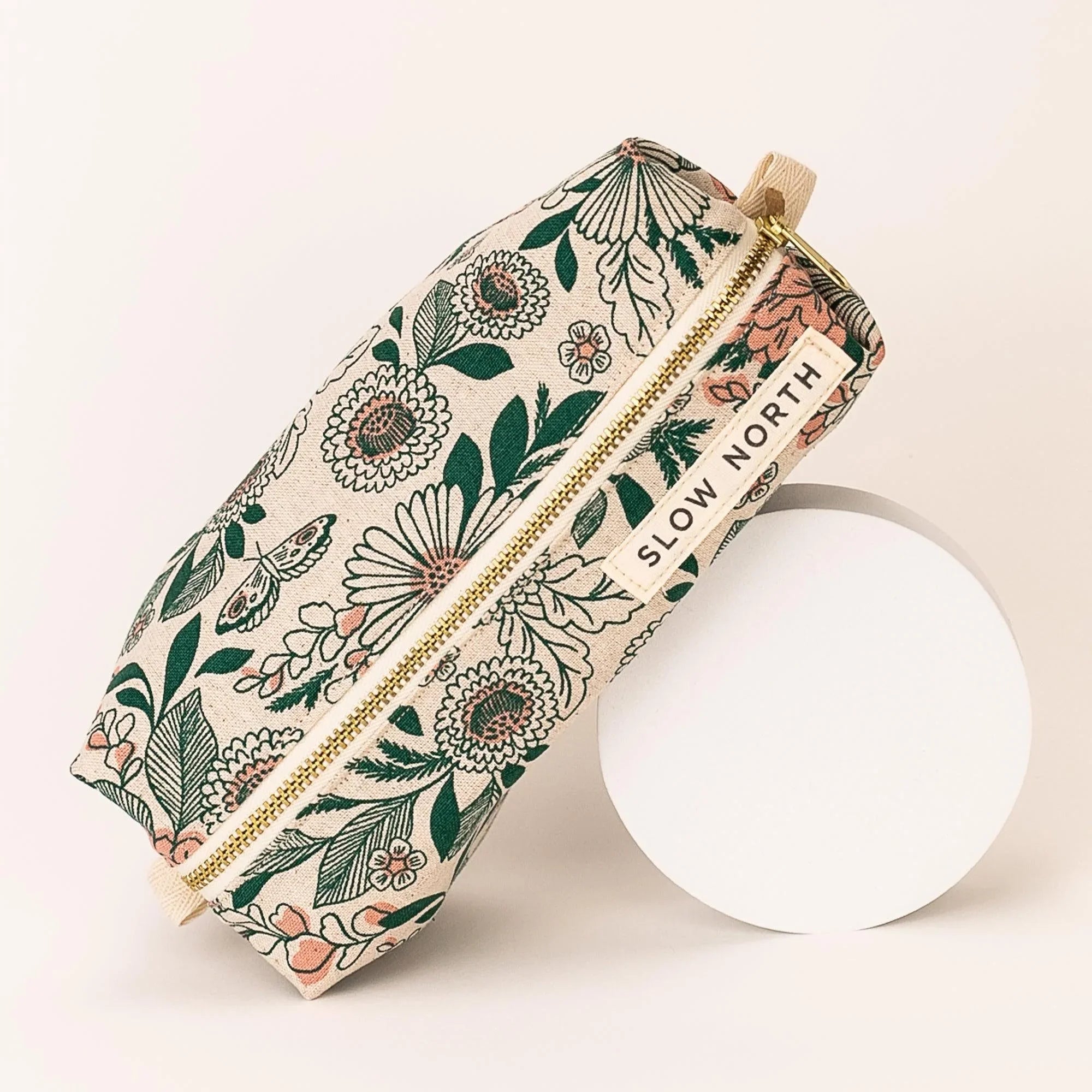 Floral patterned travel pouch with green leaves and pink flowers, gold zipper, Slow North label