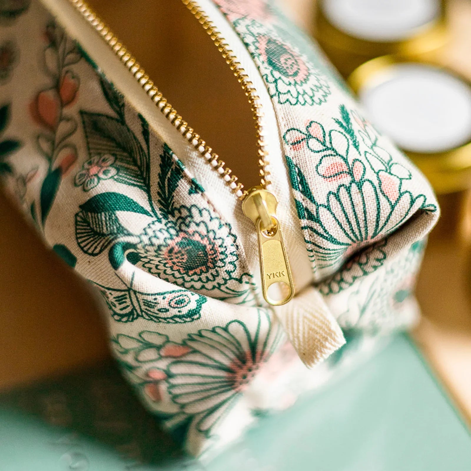 Close-up of floral fabric travel pouch with gold YKK zipper, showing green and pink flower patterns