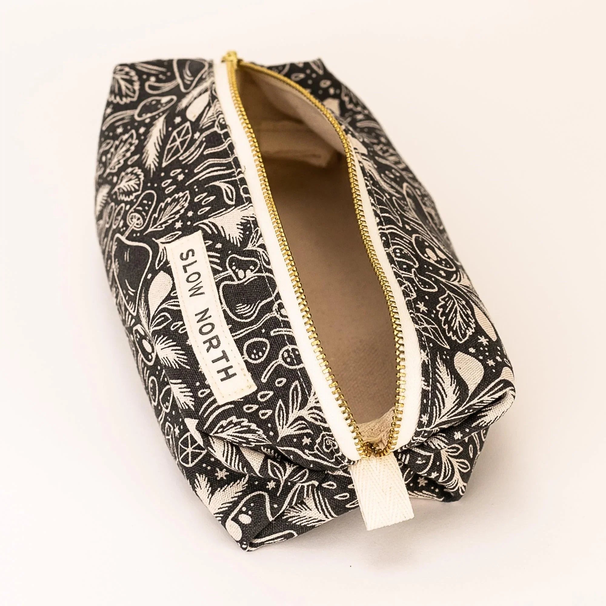 Black and white travel pouch with mystical mushroom and leaf pattern, gold zipper, Slow North label