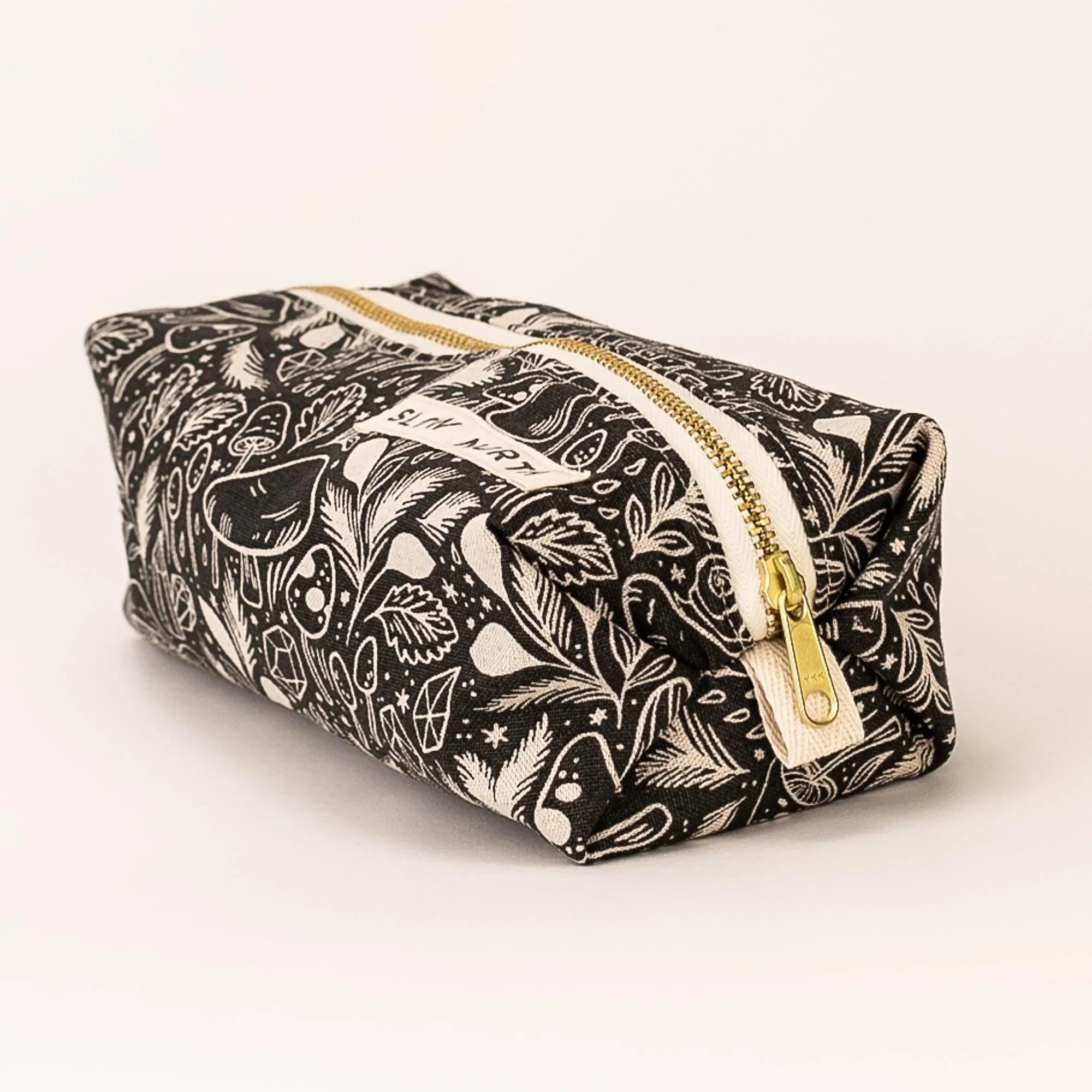 Black and white travel pouch with mystical mushroom and leaf pattern, gold zipper, Slow North label