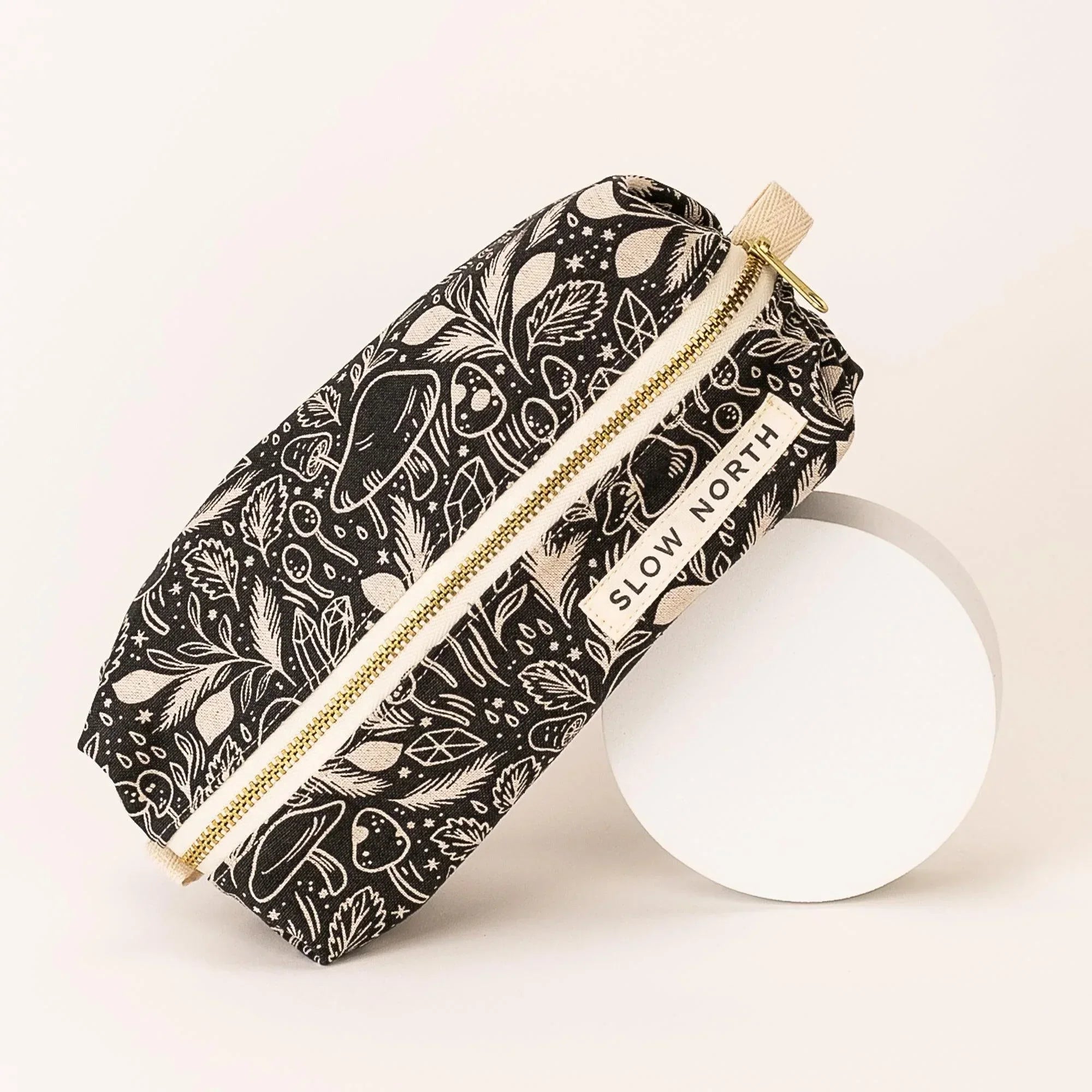 Black travel pouch with mystical mushroom and leaf pattern, gold zipper, Slow North label