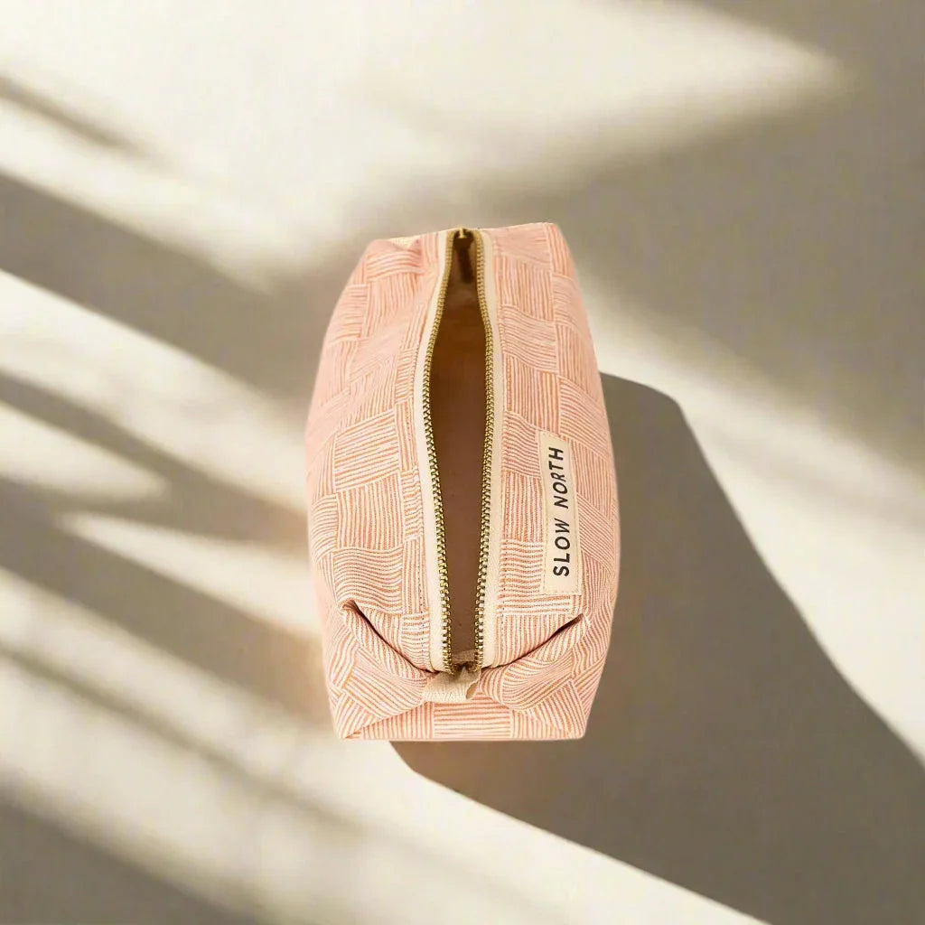 Pink textured travel pouch with gold zipper and Slow North label on beige background