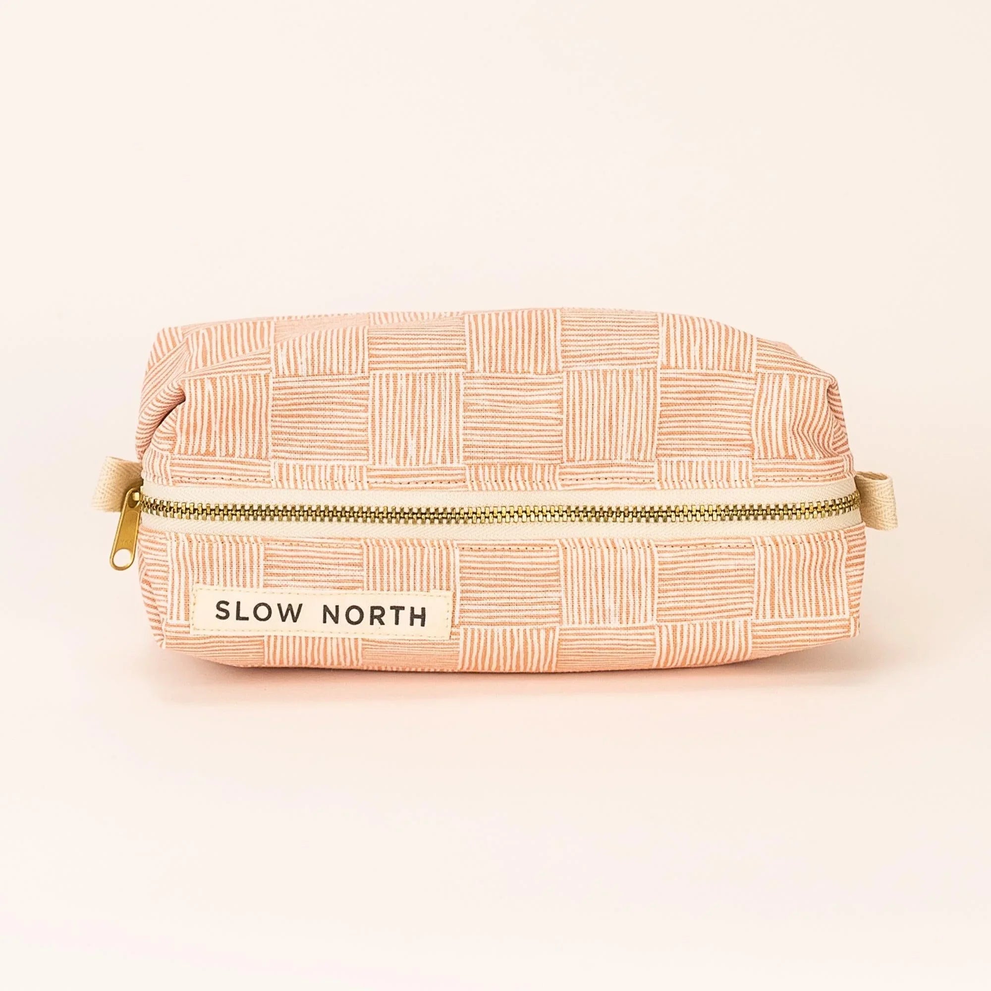 Pink patterned travel pouch with gold zipper and "SLOW NORTH" label on light background