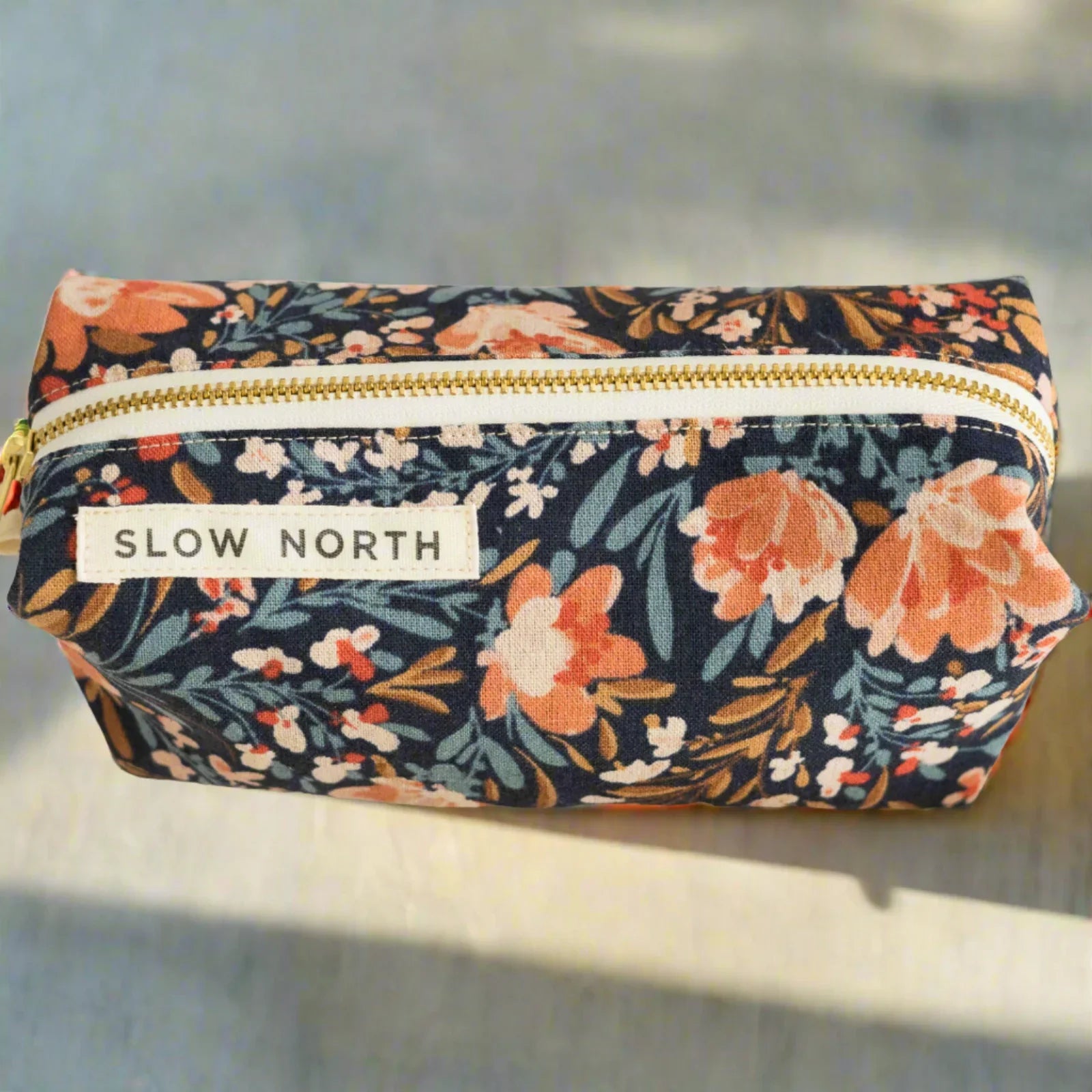 Slow North travel pouch with Pom Blossom floral pattern and gold zipper on light surface