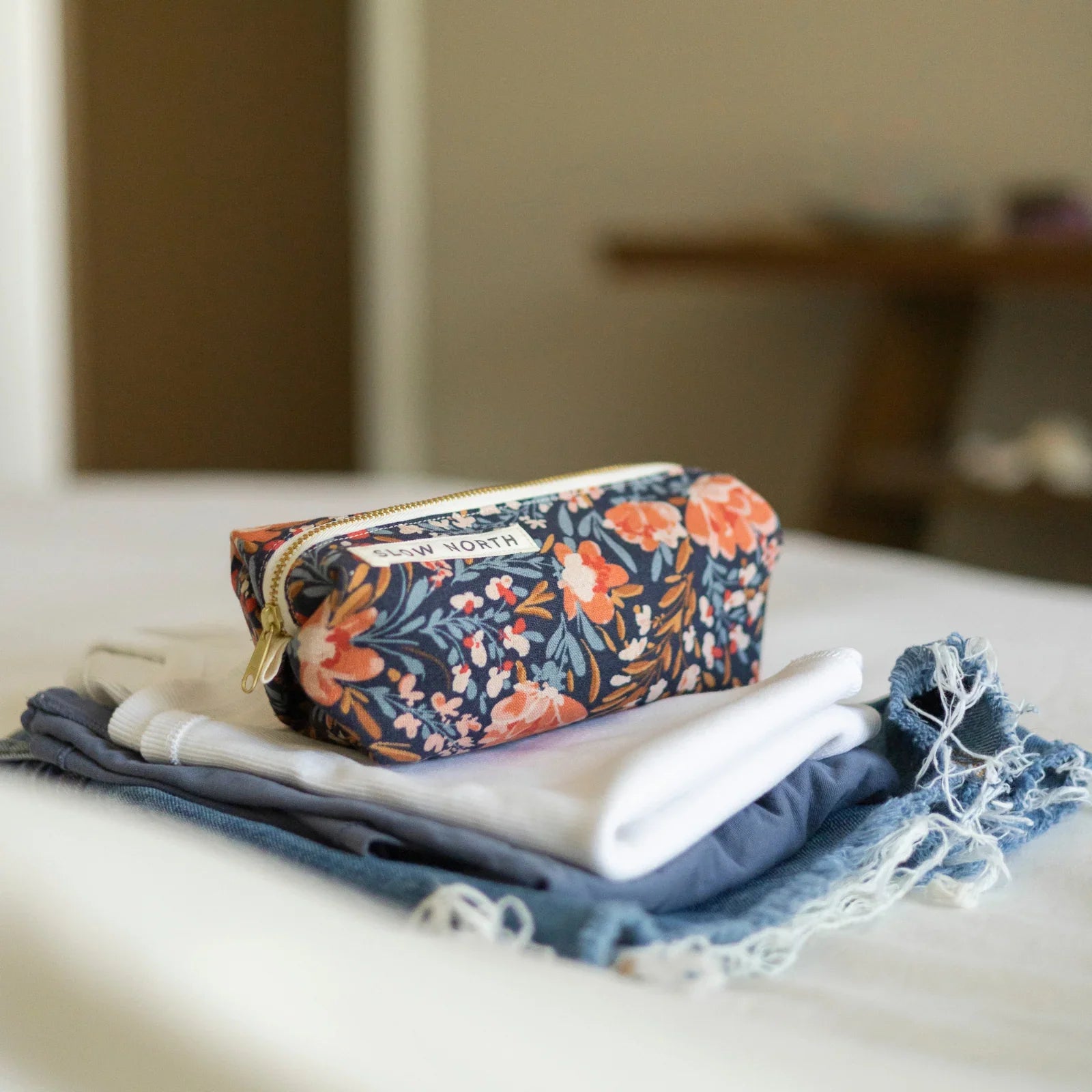 Floral travel pouch with pink and orange blossoms on navy, on folded white and denim clothes