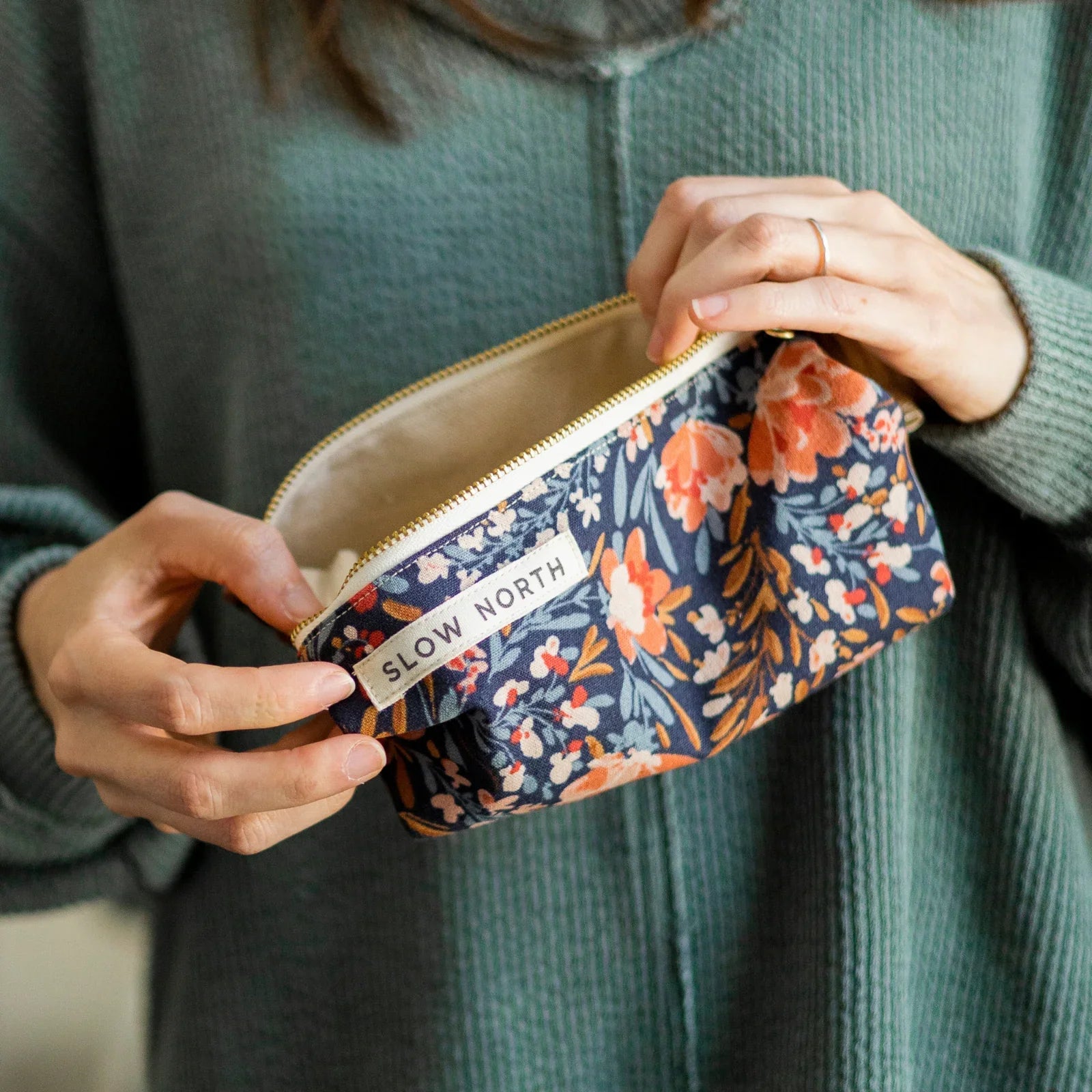 Hands holding floral travel pouch with orange and white flowers, labeled Slow North