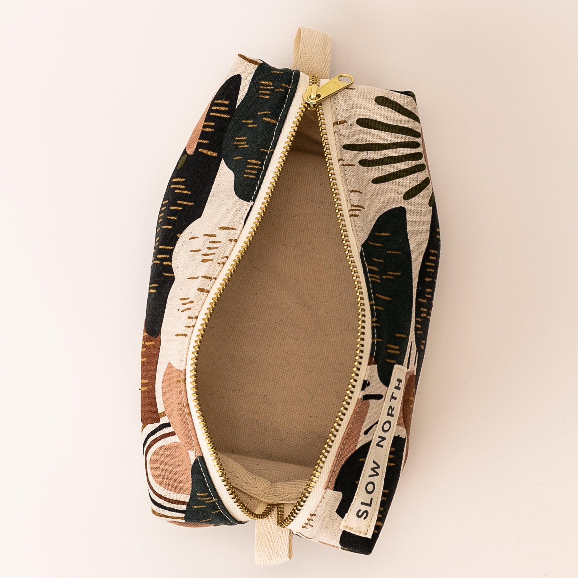 open travel pouch with abstract black, brown, beige pattern and gold zipper by Slow North