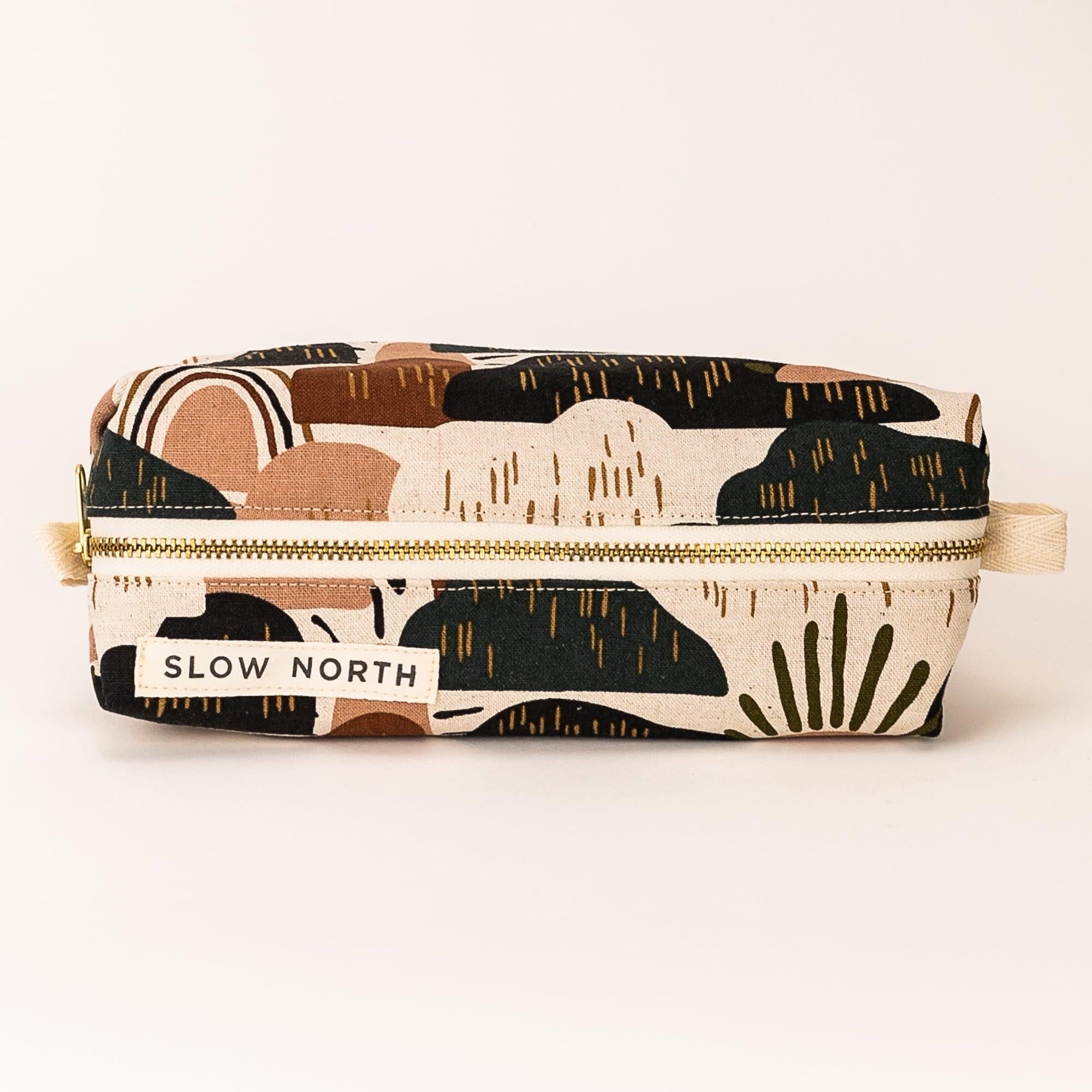 Slow North travel pouch with abstract earthy pattern and gold zipper on white background