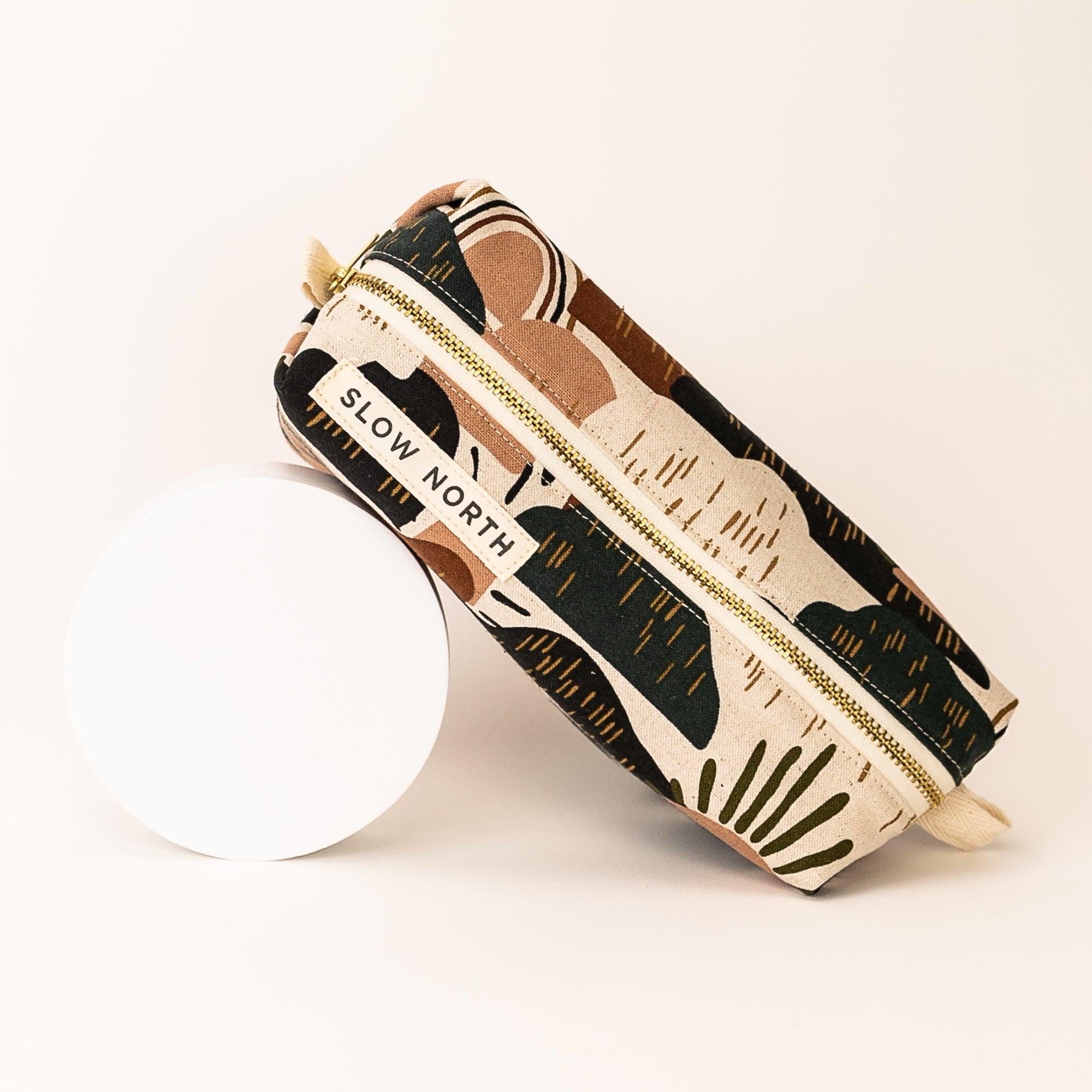 Slow North canvas travel pouch with abstract earth-toned nature print and gold zipper