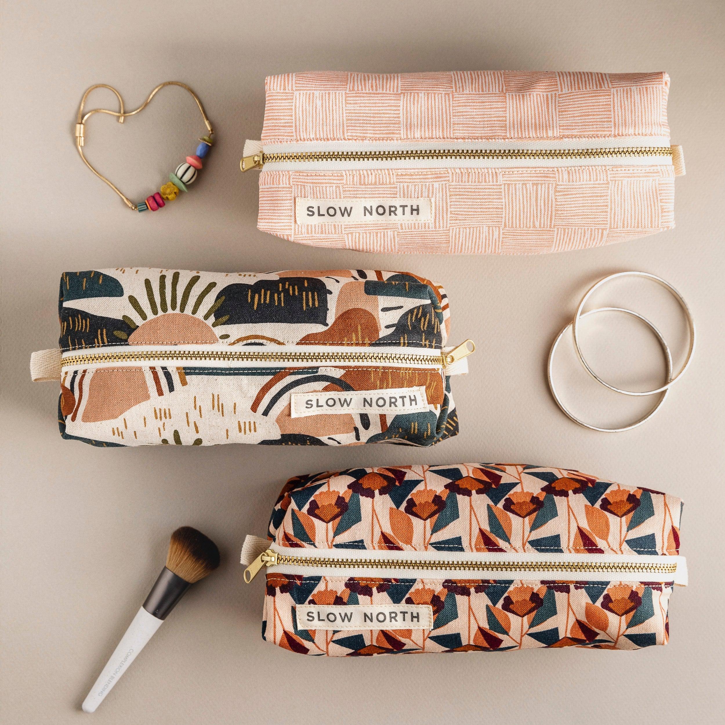 Three Slow North travel pouches with geometric and floral patterns, displayed with jewelry and makeup brush