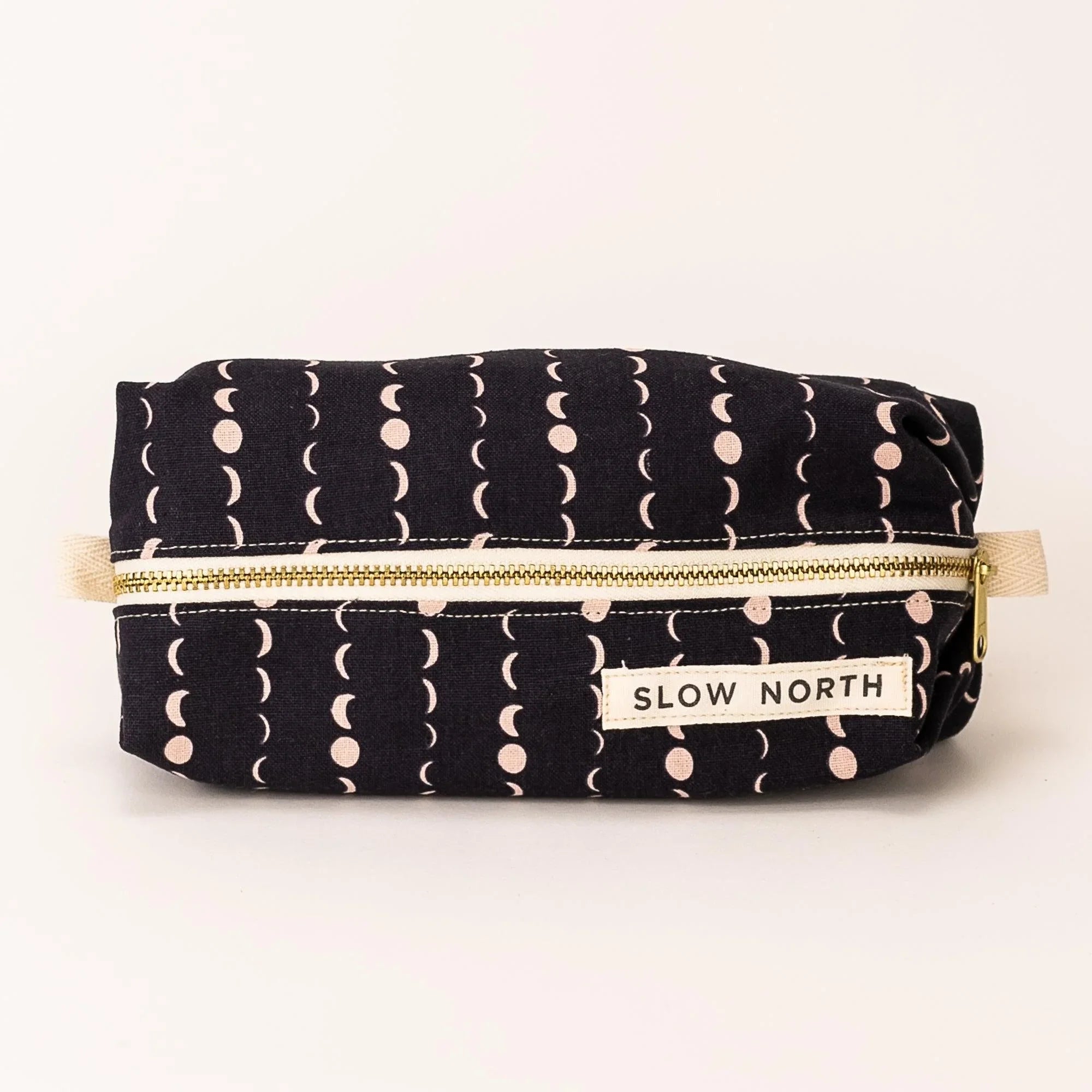 Black travel pouch with moon phase pattern and gold zipper labeled Slow North
