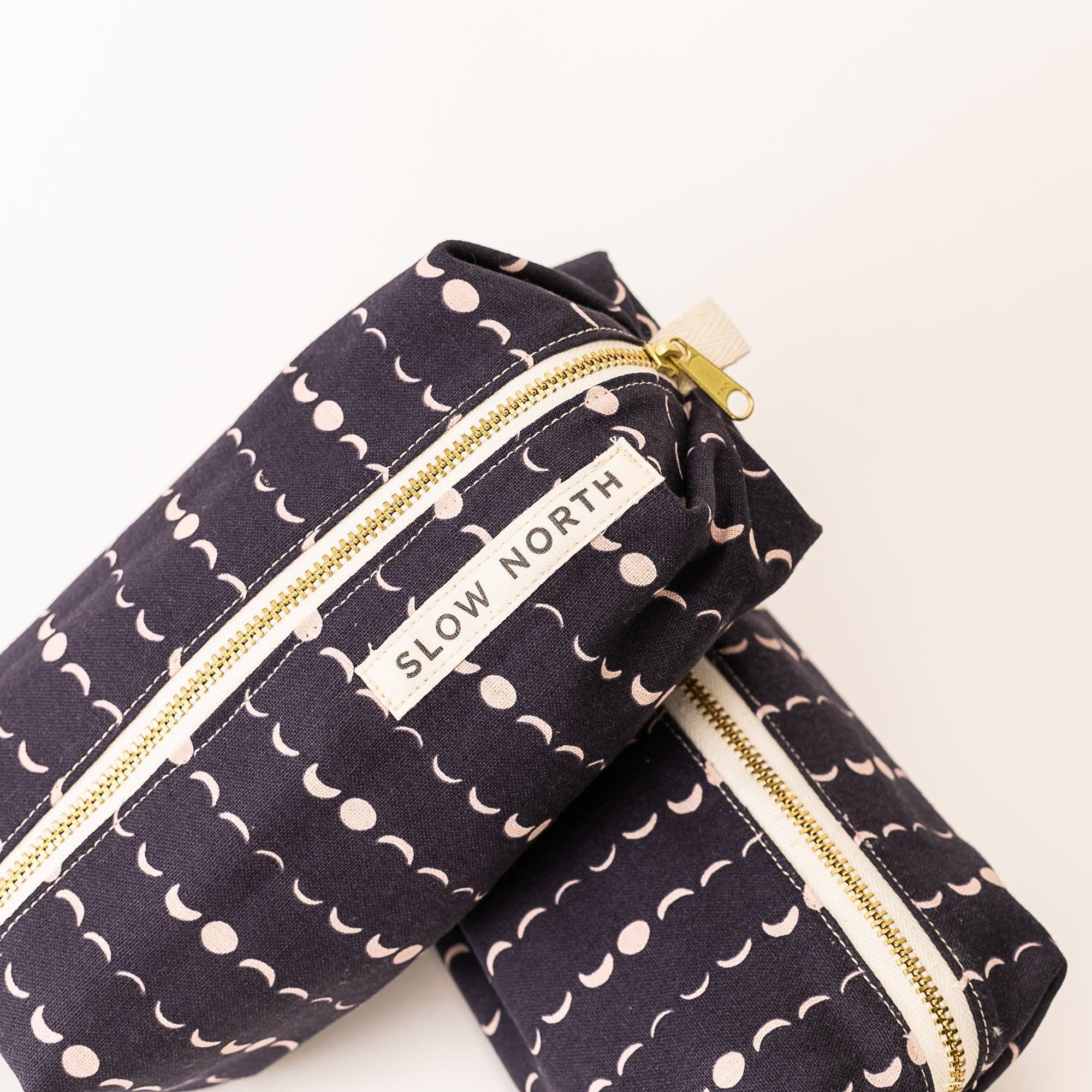 Two black fabric travel pouches with moon phase pattern and gold zippers, labeled Slow North