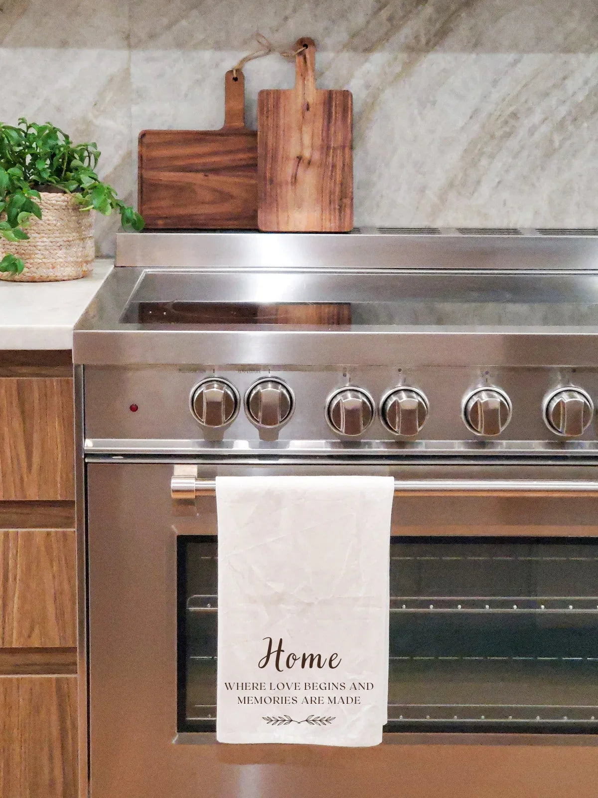 White kitchen tea towel with home quote hanging on stainless steel oven handle in modern kitchen