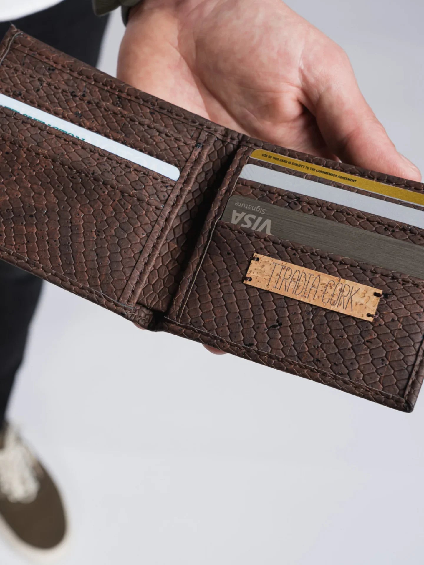 Hand holding a brown textured eco-friendly wallet with visible cards and a cork label.