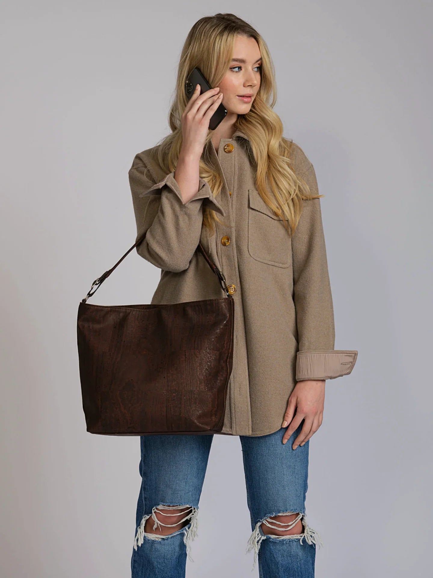 Woman in beige jacket and ripped jeans holding a brown tote bag, Qu!rk Boutique style