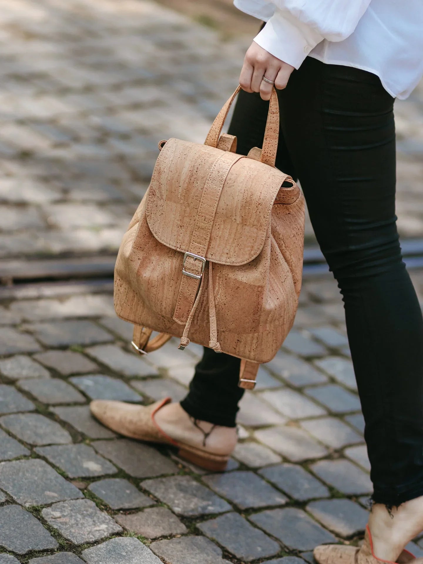 Woman holding cork backpack and wearing sustainable cork shoes on cobblestone street