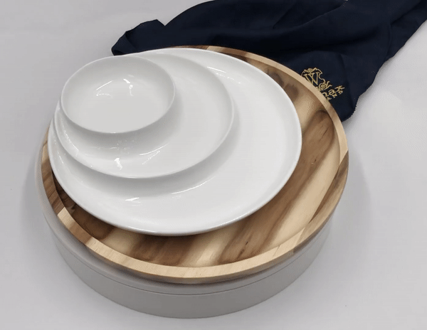 Stack of white ceramic plates and bowls on a round wooden and gray serving tray with a dark cloth napkin