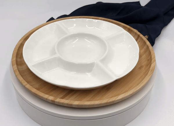 White ceramic divided serving platter on round bamboo tray with navy cloth on white background