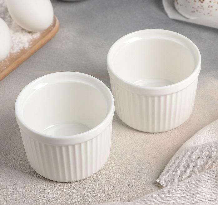 Pair of white ceramic ramekins with ribbed sides on a light countertop, kitchen baking scene