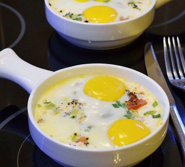 Baked eggs with vegetables in white oven-safe ramekins, served on a stovetop