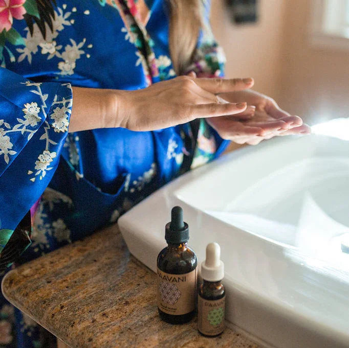 Woman in blue floral robe applying face oil by sink, Qu!rk Boutique organic skincare products