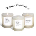 Three lit soy candles in frosted glass jars labeled Embers Leather, Orange Clove, Moonglow by Slow North