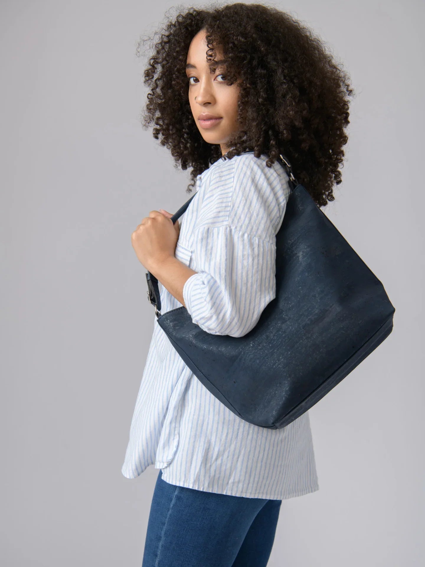 Woman wearing striped blouse and jeans with large navy vegan shoulder bag from Qu!rk Boutique
