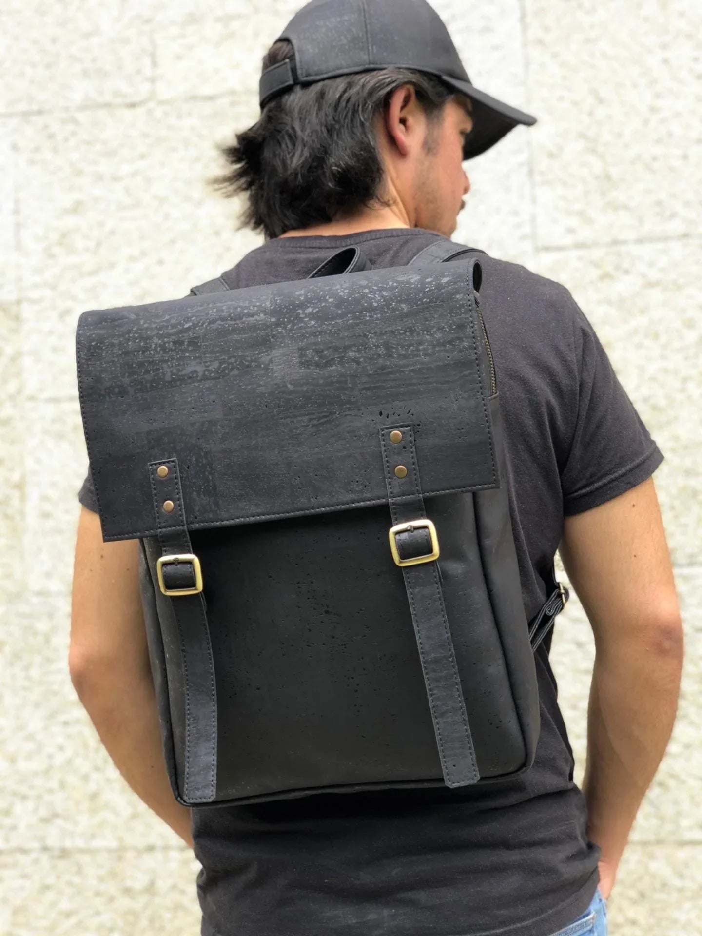 Man wearing a black cork vegan leather backpack with brass buckles, minimalist urban style