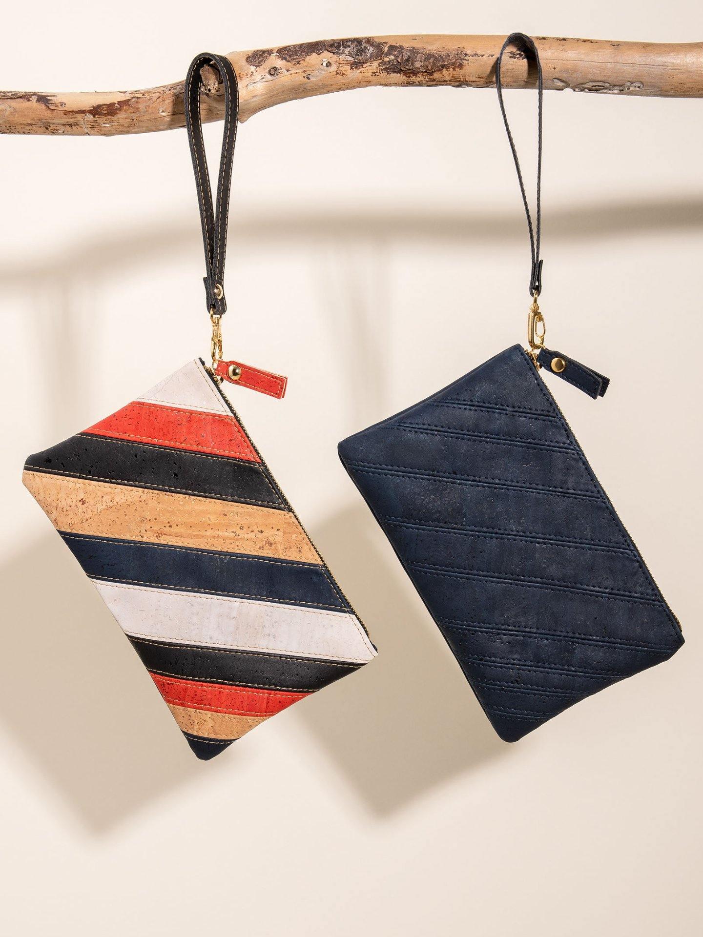 Two artist-designed wristlet bags, one striped and one navy, hanging on a wooden branch.