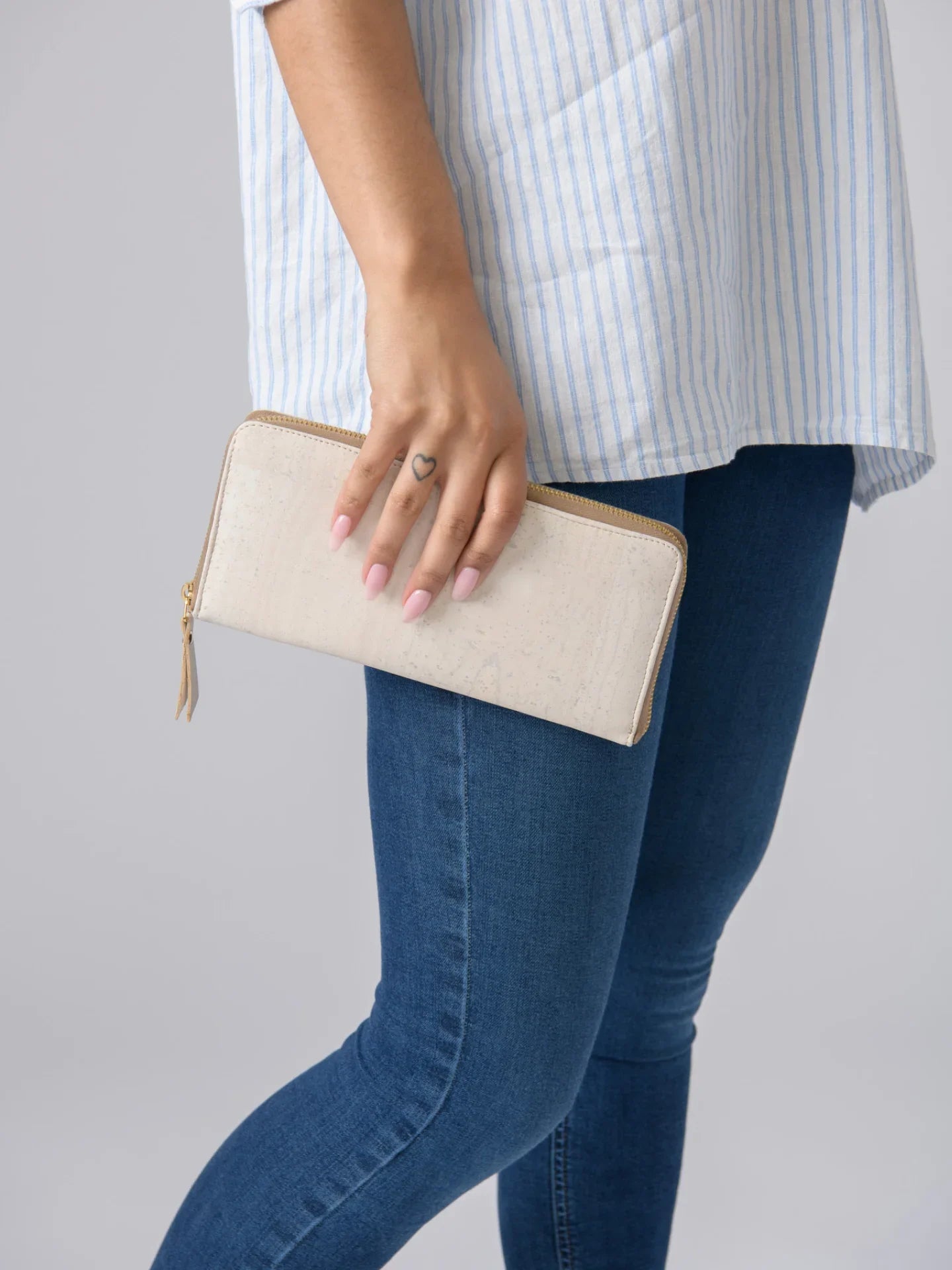 Woman holding cream vegan wallet, wearing jeans and striped top, Qu!rk Boutique accessory